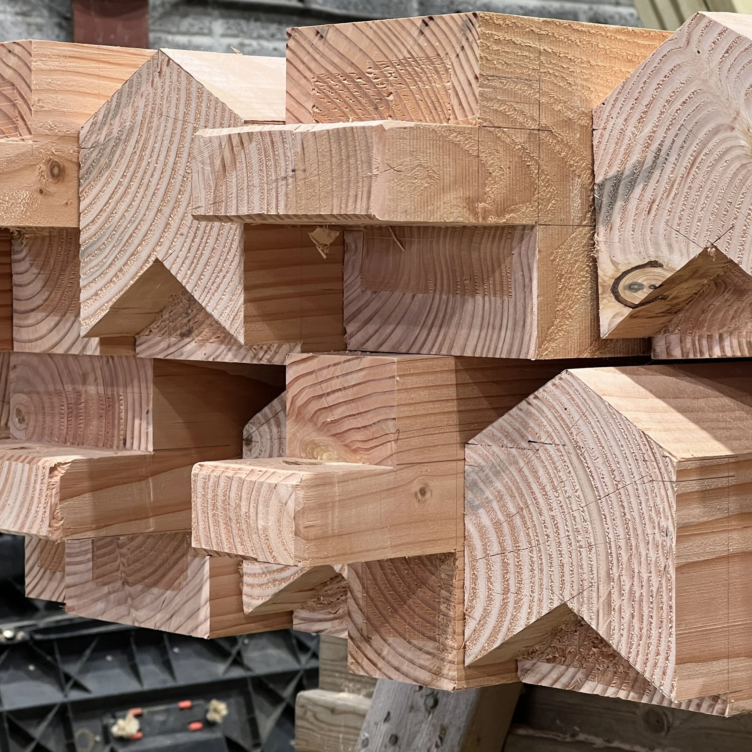 Douglas Fir timbers stacked in workshop with joints cut on ends in interesting shapes.