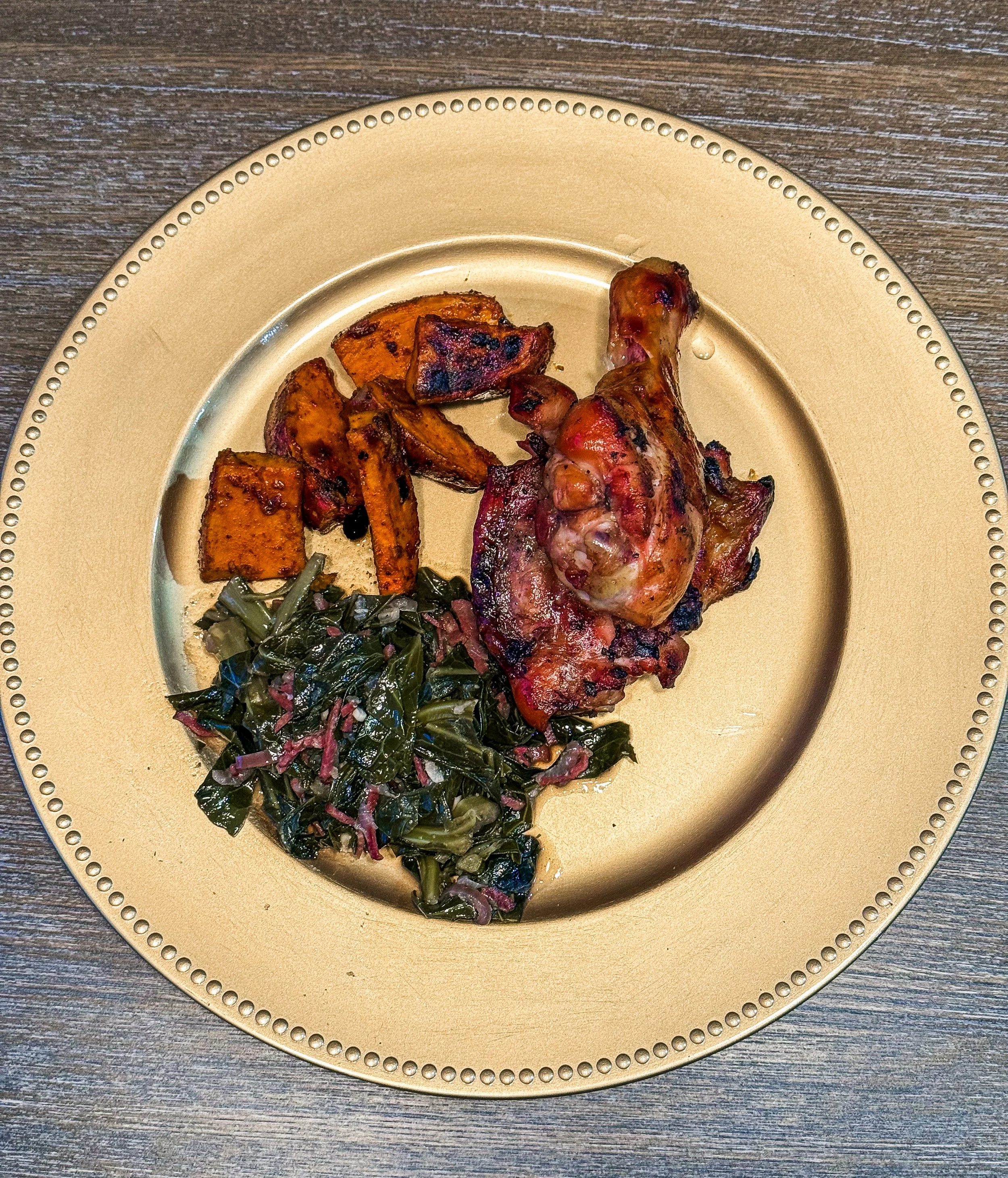 braised chicken leg with collard greens and sweet potato wedges on a plate