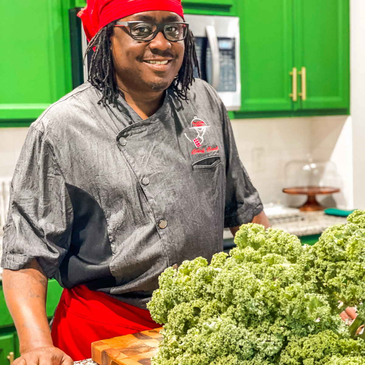 Chef Carl Welch Jr standing at a kitchen counter with a large head of kale on a cutting board