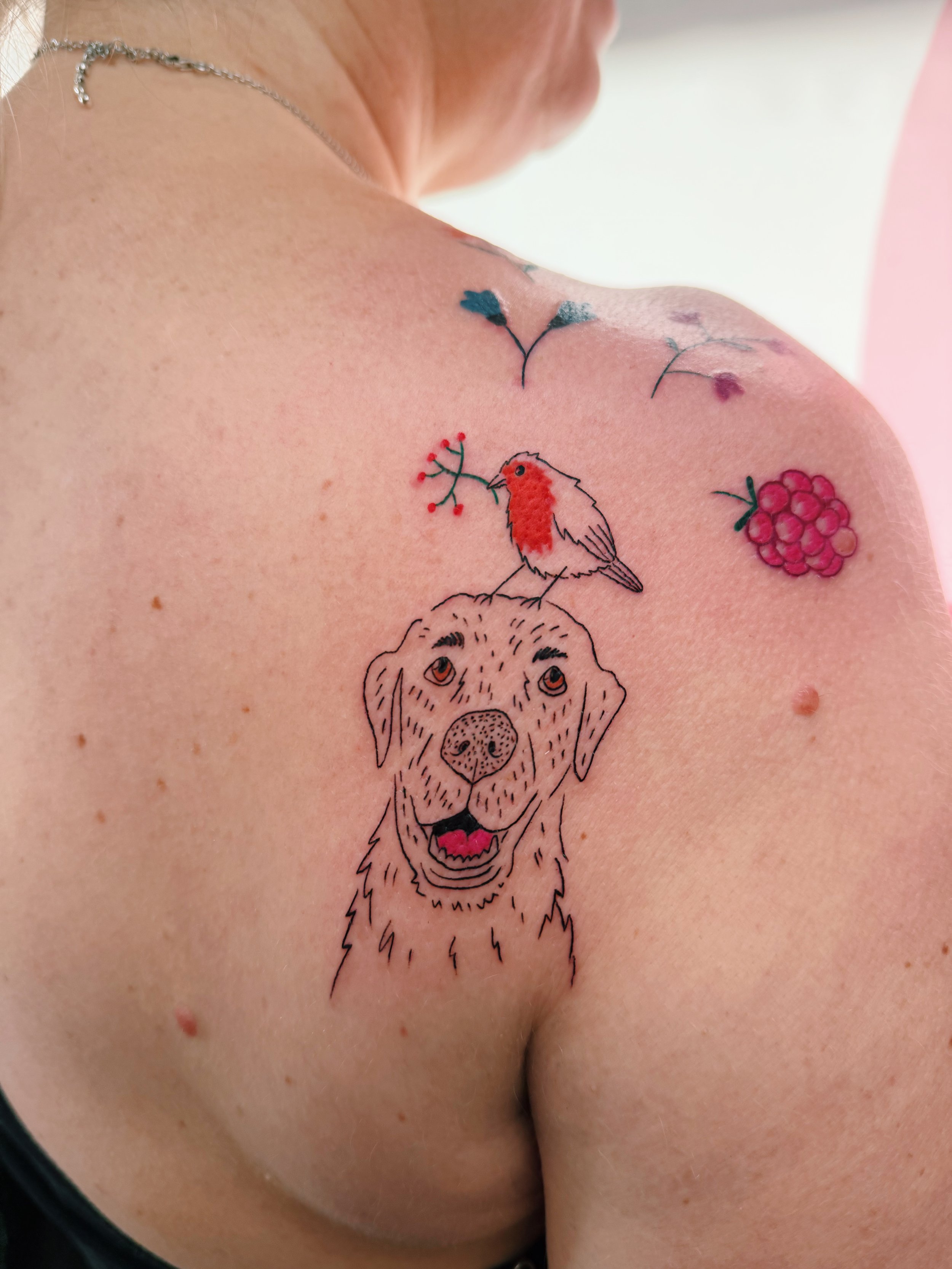 a custom tattoo of a dog with a robin on his head, flowers and berries