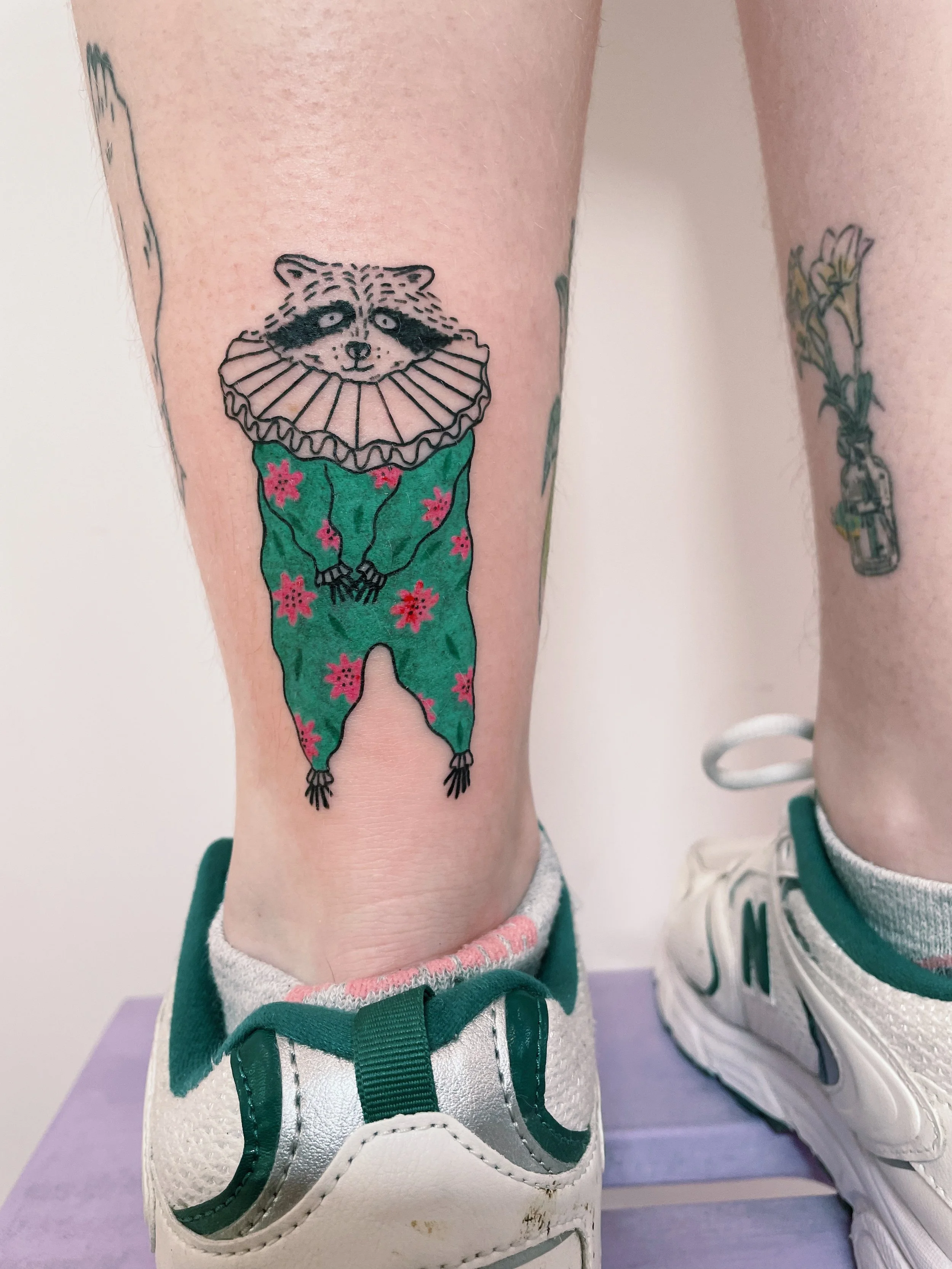 a custom tattoo of a raccoon wearing a colorful clown costume