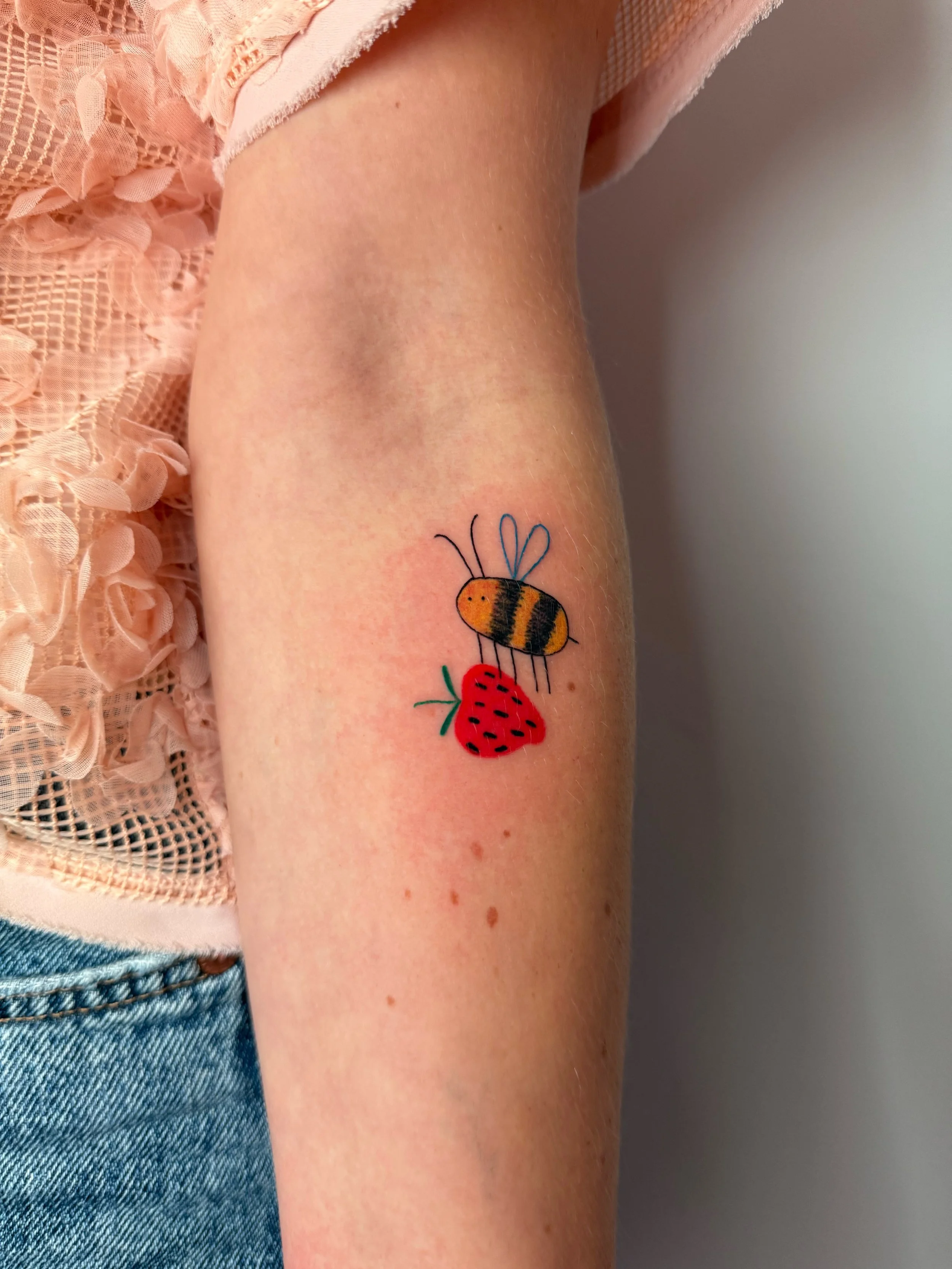 a custom tattoo of a cute bee holding a strawberry