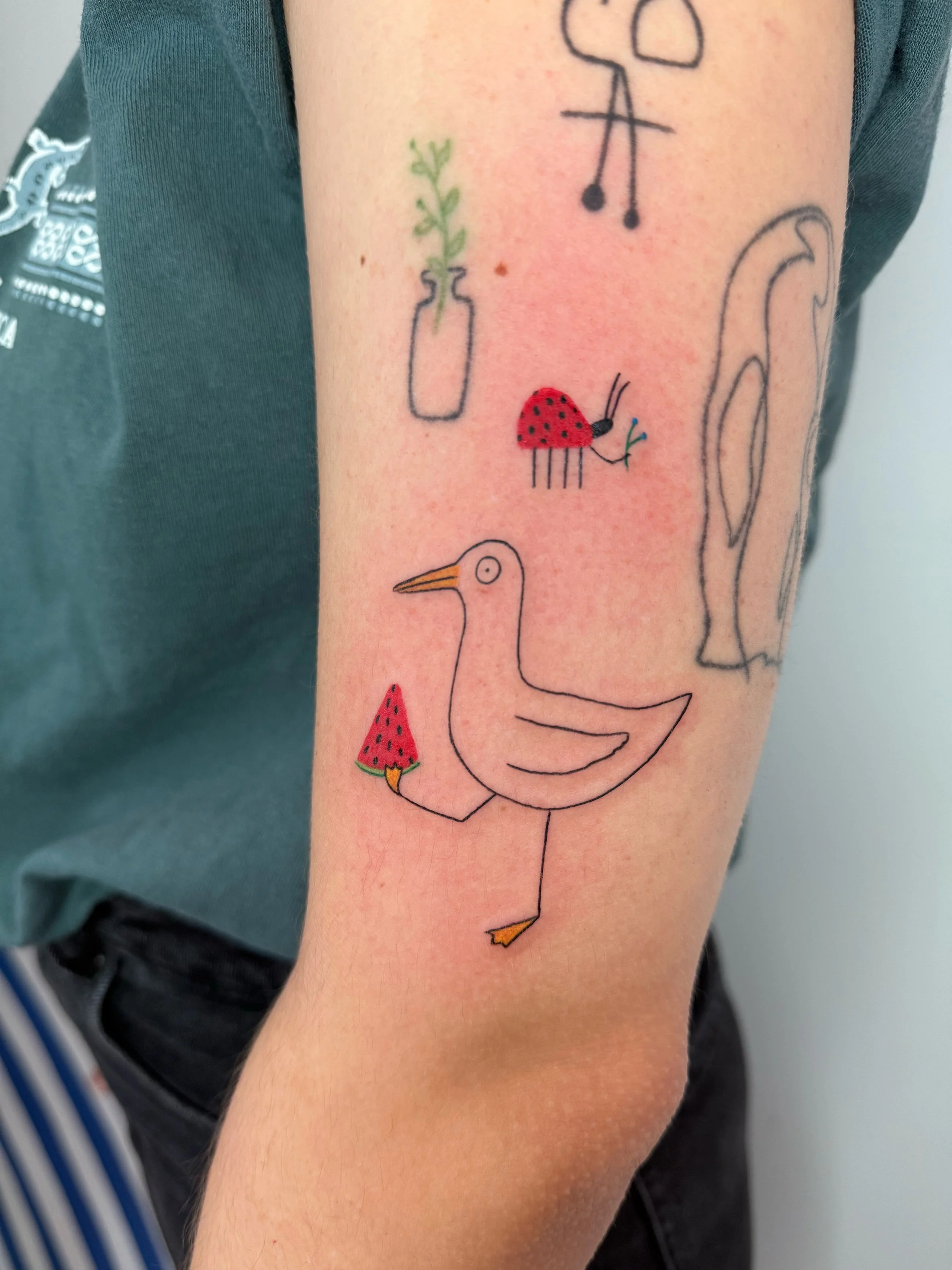 a custom tattoo of a silly seagull holding a slice of a watermelon, and a tattoo of a ladybug holding a berry branch