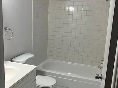 A bathroom with a white bathtub, a toilet, a sink, and tiled walls.