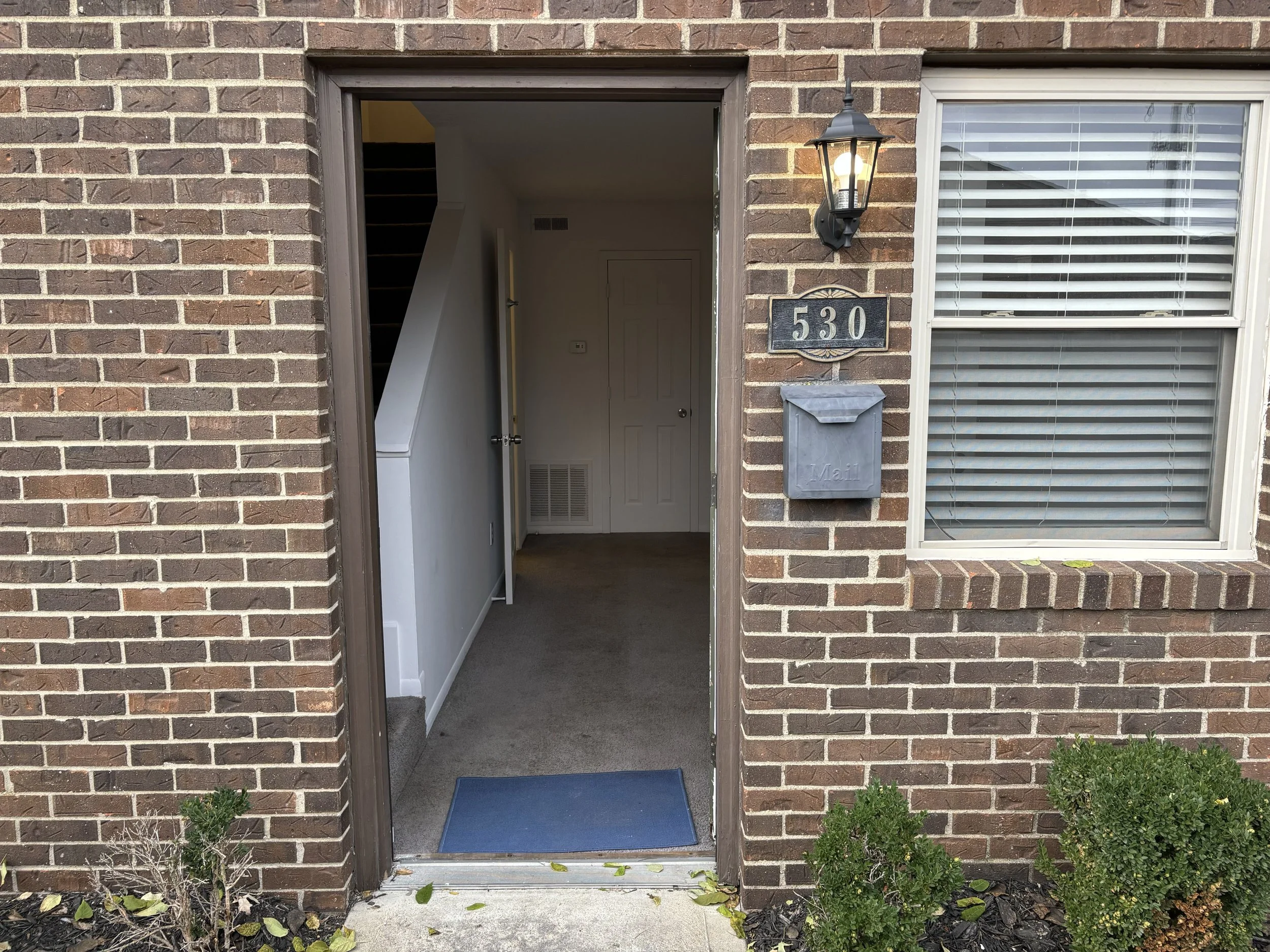 Entrance to a brick house with house number 530, a wall-mounted lantern, a mailbox, and a window with blinds. There are small bushes at the front.