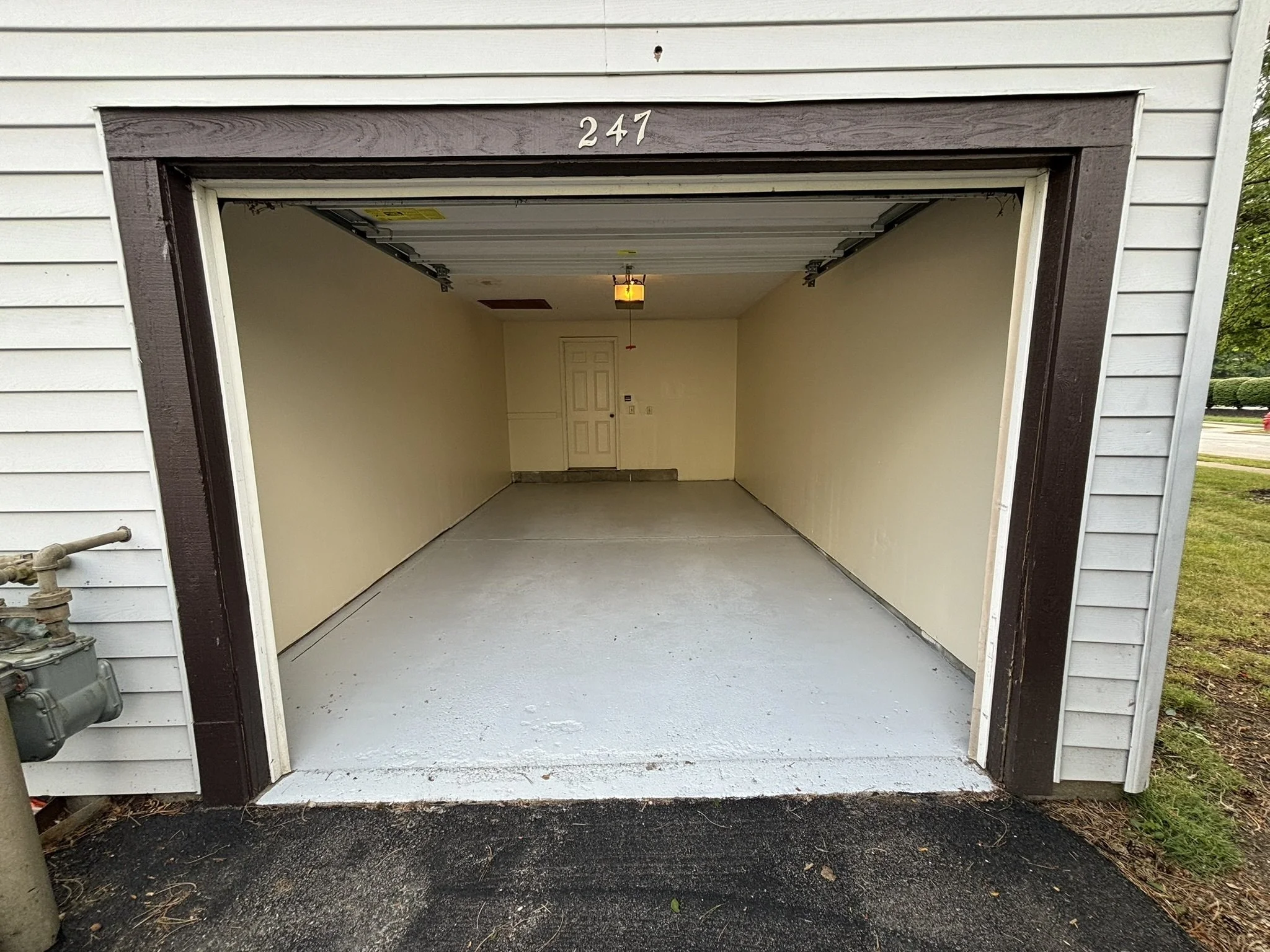 Empty residential garage with white walls, a ceiling light, and a door at the back wall.