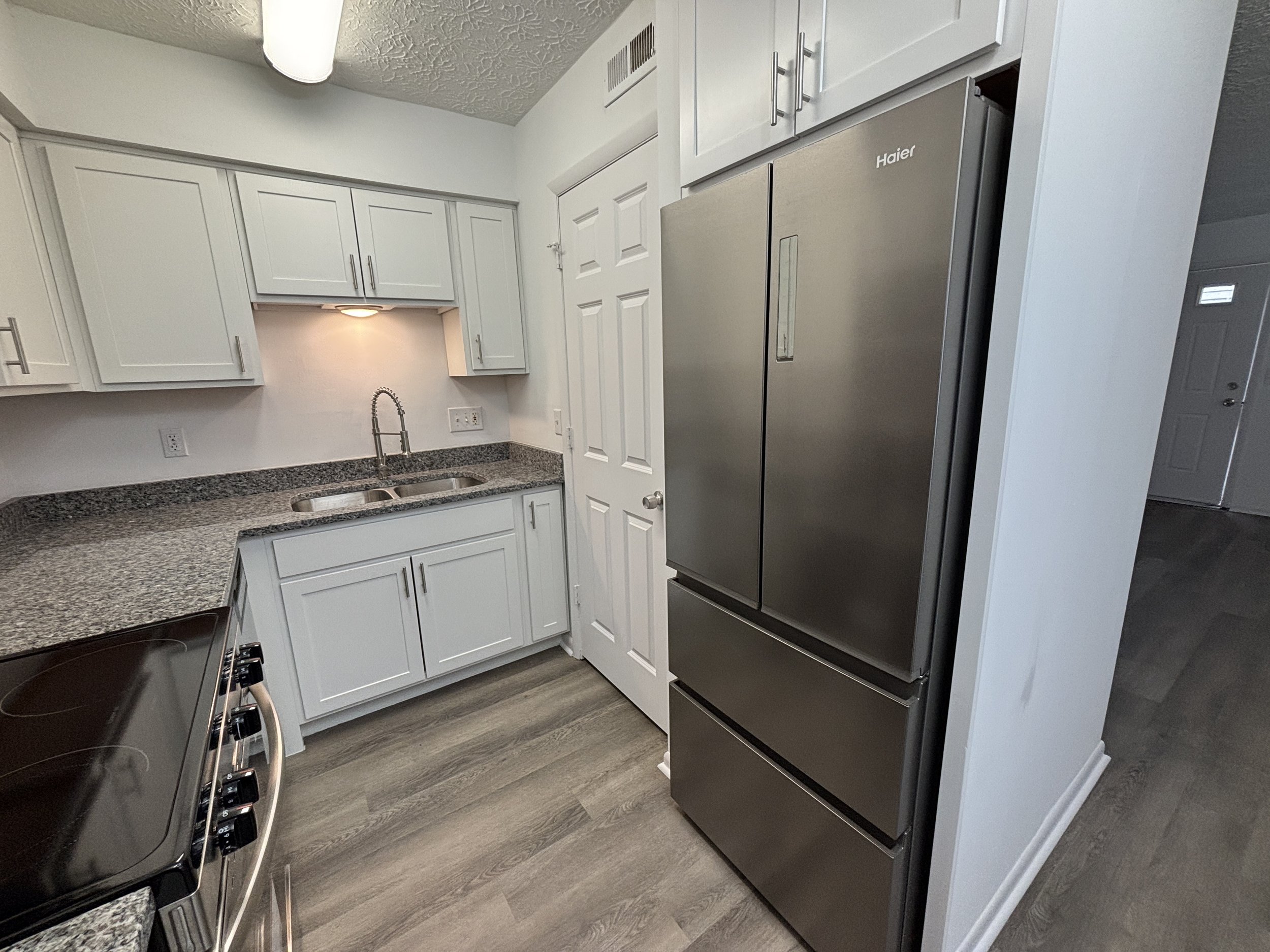 A modern kitchen with white cabinets, a granite countertop, a stainless steel refrigerator, and a sink with a gooseneck faucet.