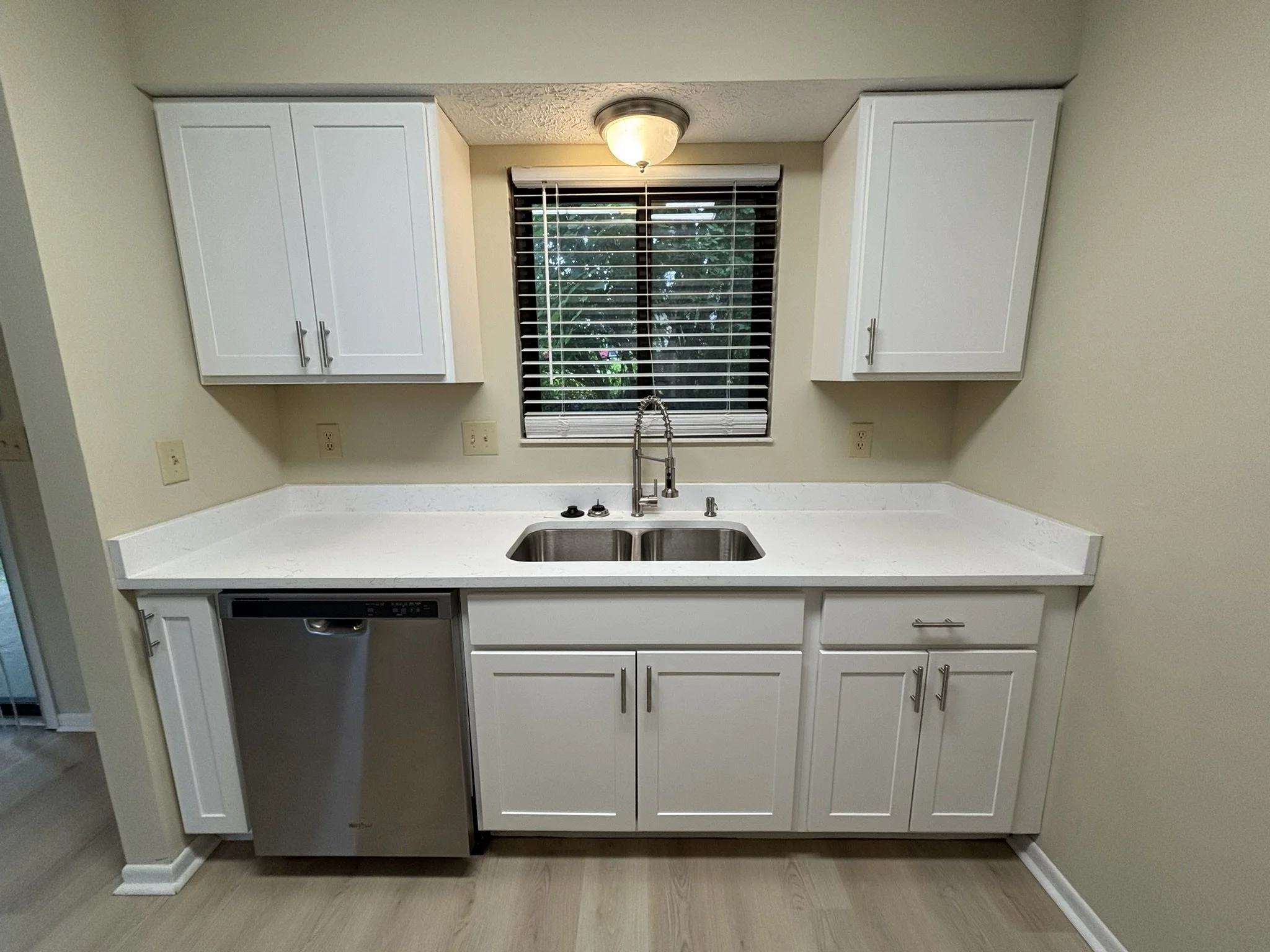 Kitchen with white cabinets, a window with blinds, a stainless steel sink, a dishwasher, and beige walls.