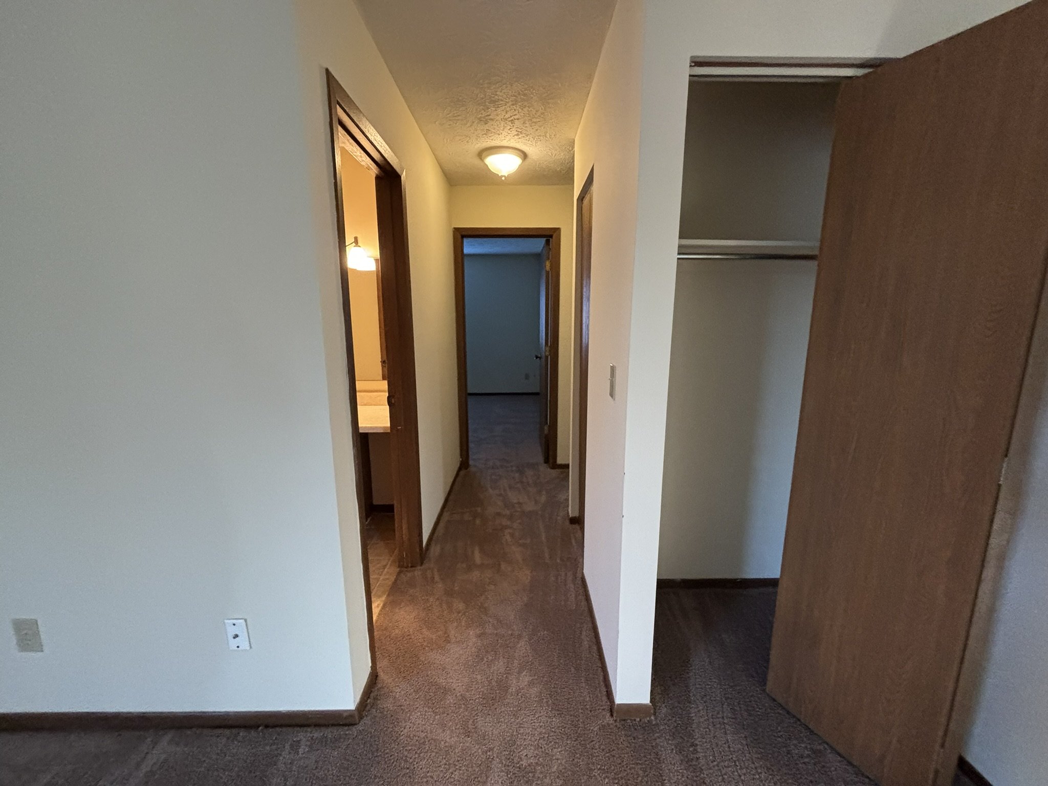 Interior of an empty room with a hallway, open closet with wooden doors, and doorways leading to other rooms.