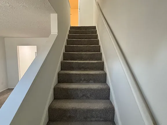 Indoor staircase with gray carpeted steps and white walls.