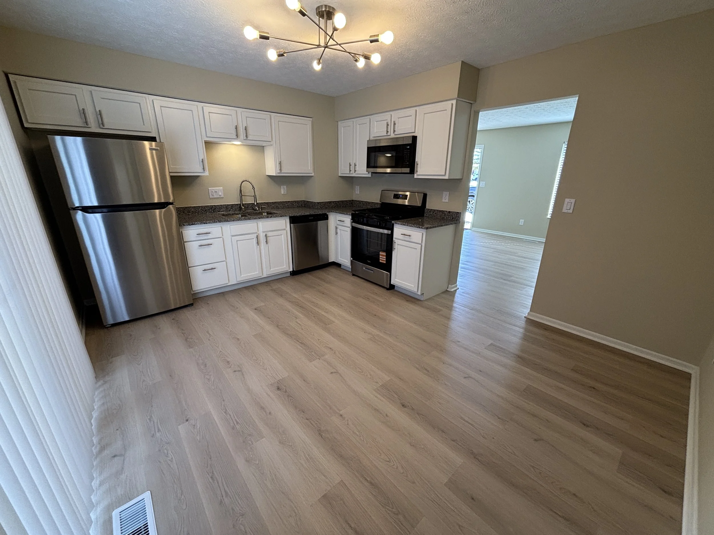 Kitchen with white cabinets, stainless steel refrigerator, microwave, and stove, granite countertops, hardwood floors, and a modern light fixture on the ceiling.