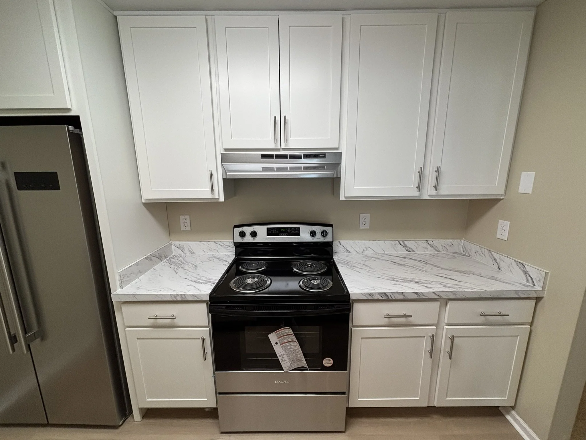 Kitchen with white cabinets, marble countertop, stainless steel refrigerator, and black electric stove with oven.