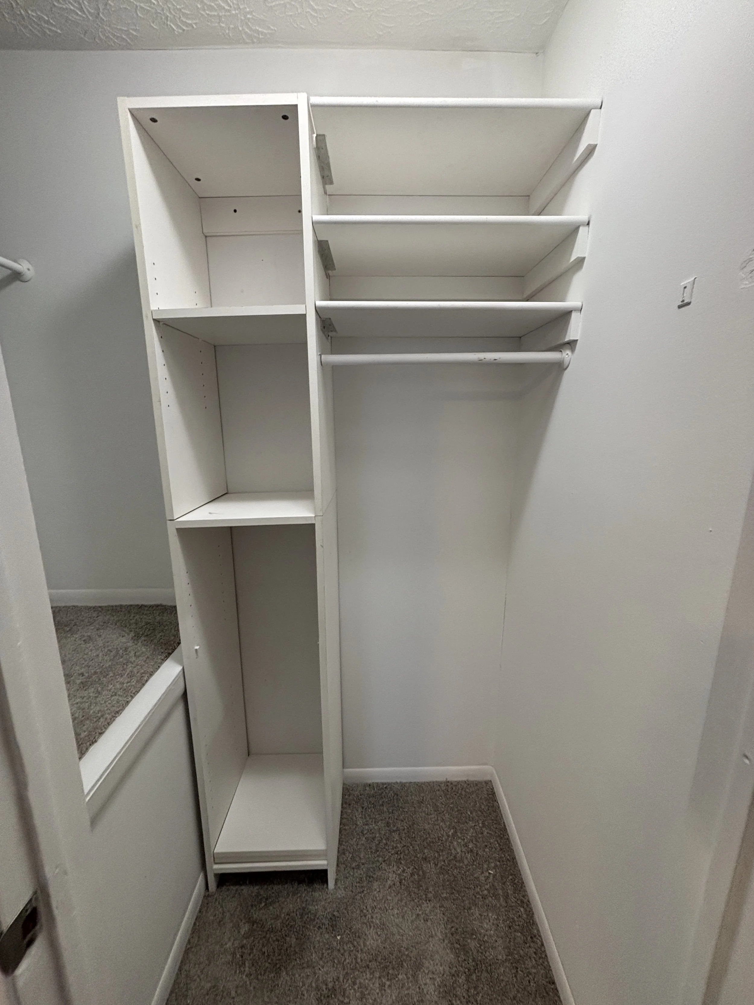 Empty white closet with several shelves and a hanging rod, with beige carpeted floor.