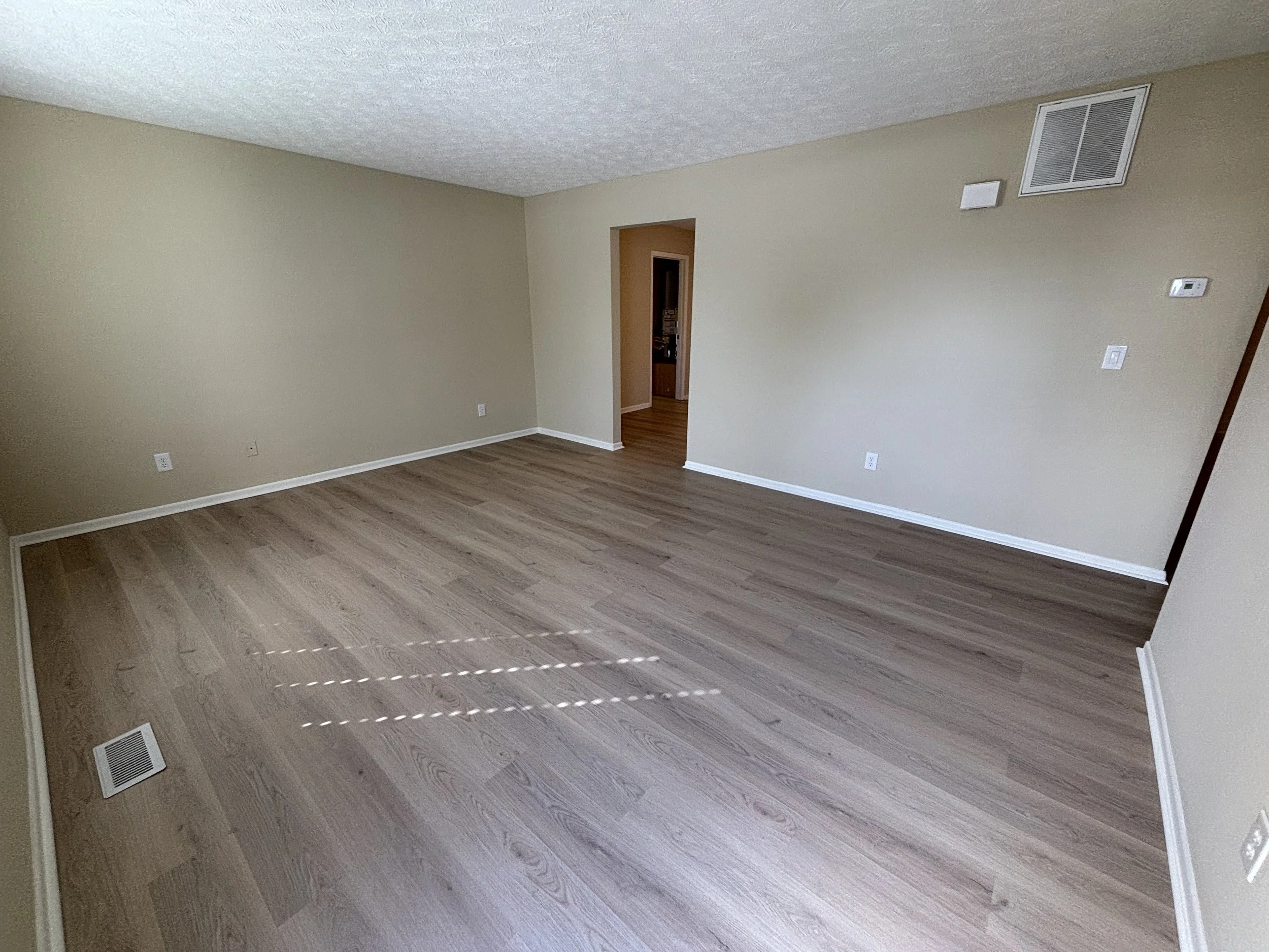 Empty living room with beige walls, wood flooring, and a doorway leading to another room.