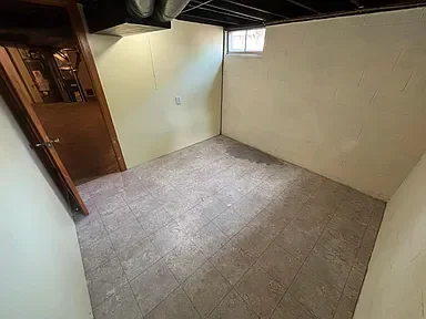 Empty room with beige tiled floor, pale yellow walls, a small window, and an open door.