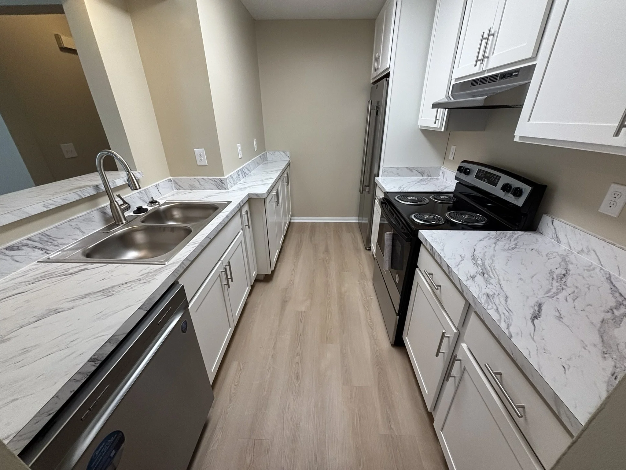 Modern kitchen with white cabinets, marble countertops, stainless steel sink, black stove, and light wood flooring.