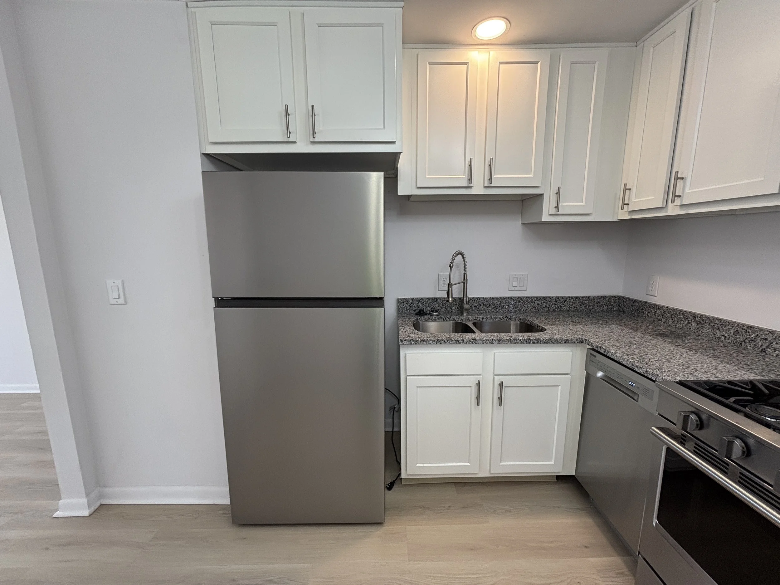 Modern kitchen with white cabinets, a stainless steel refrigerator, granite countertop, a sink with a gooseneck faucet, and a stainless steel stove.