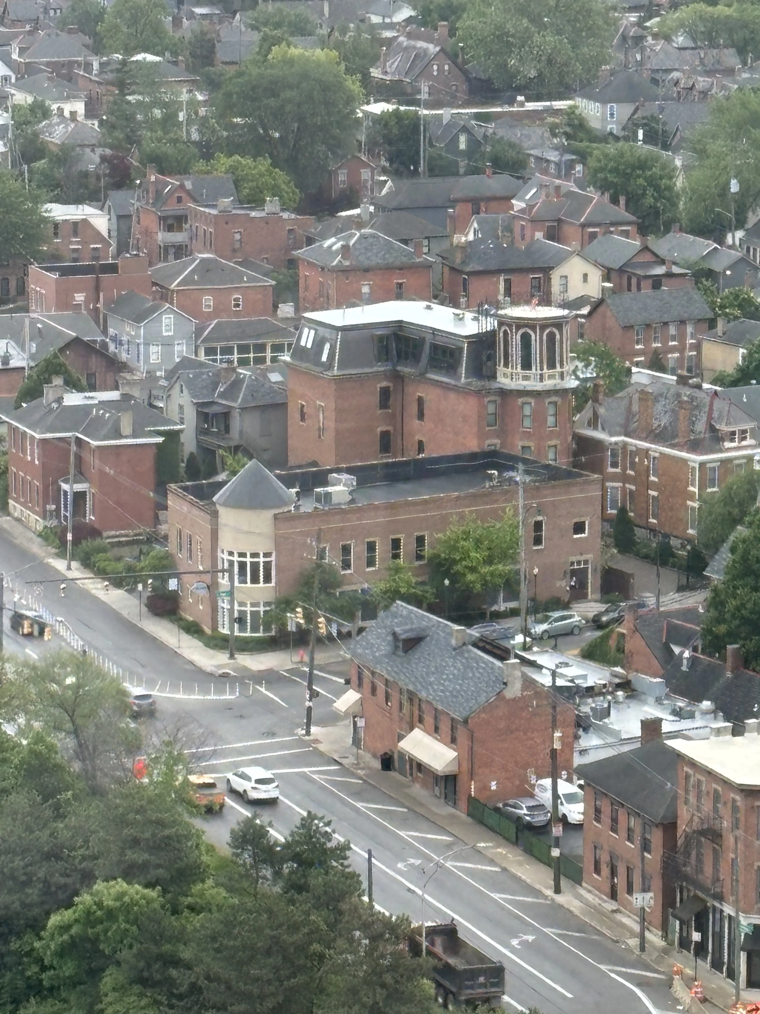 Aerial view of a neighborhood with closely spaced brick buildings, trees, and streets with parked cars.