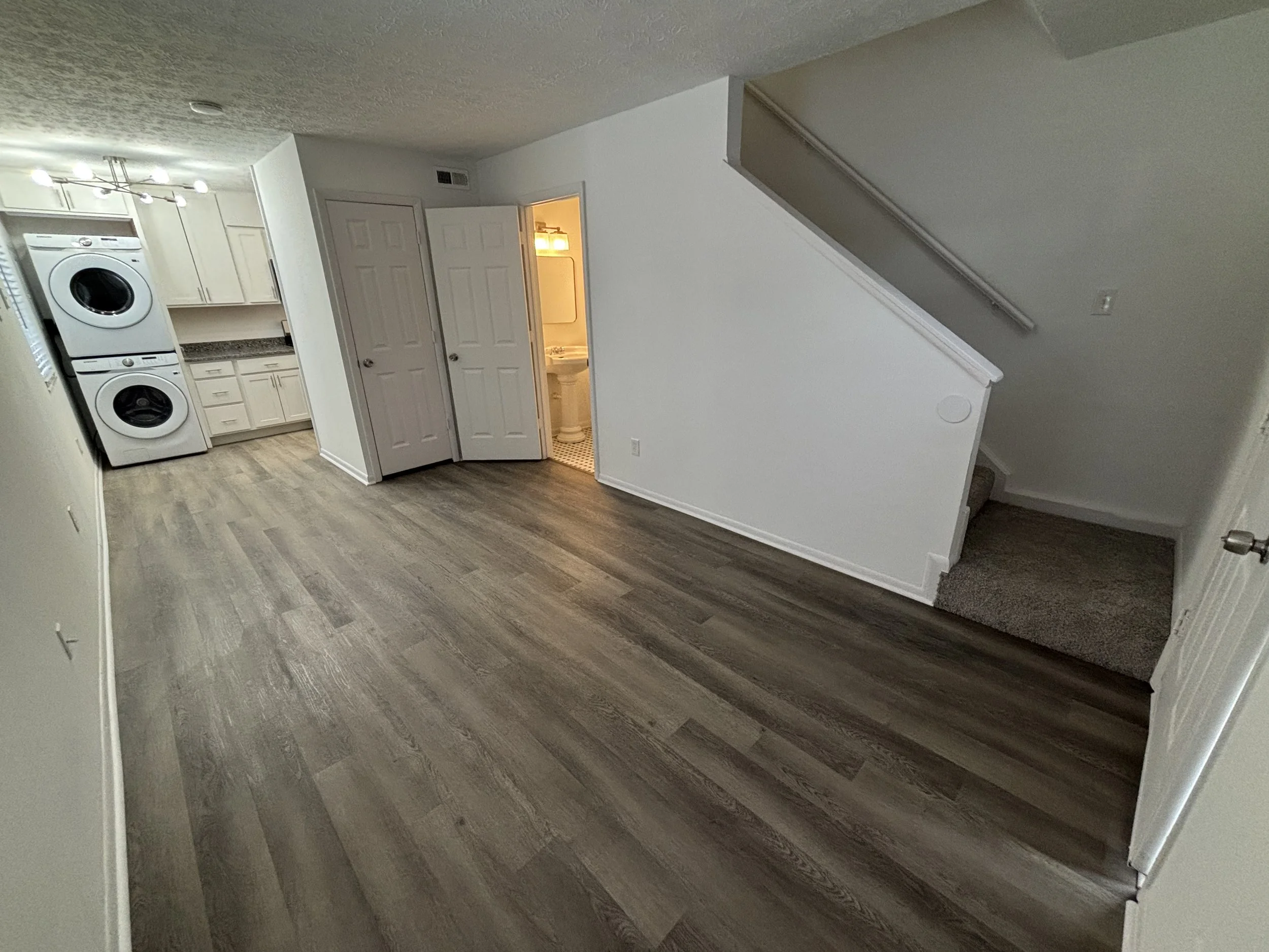 Empty room with a laundry area on the left, a small bathroom with a sink and mirror in the middle, and a staircase on the right.
