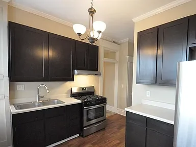 Kitchen with dark cabinets, stainless steel stove and refrigerator, white countertops, and a chandelier overhead.