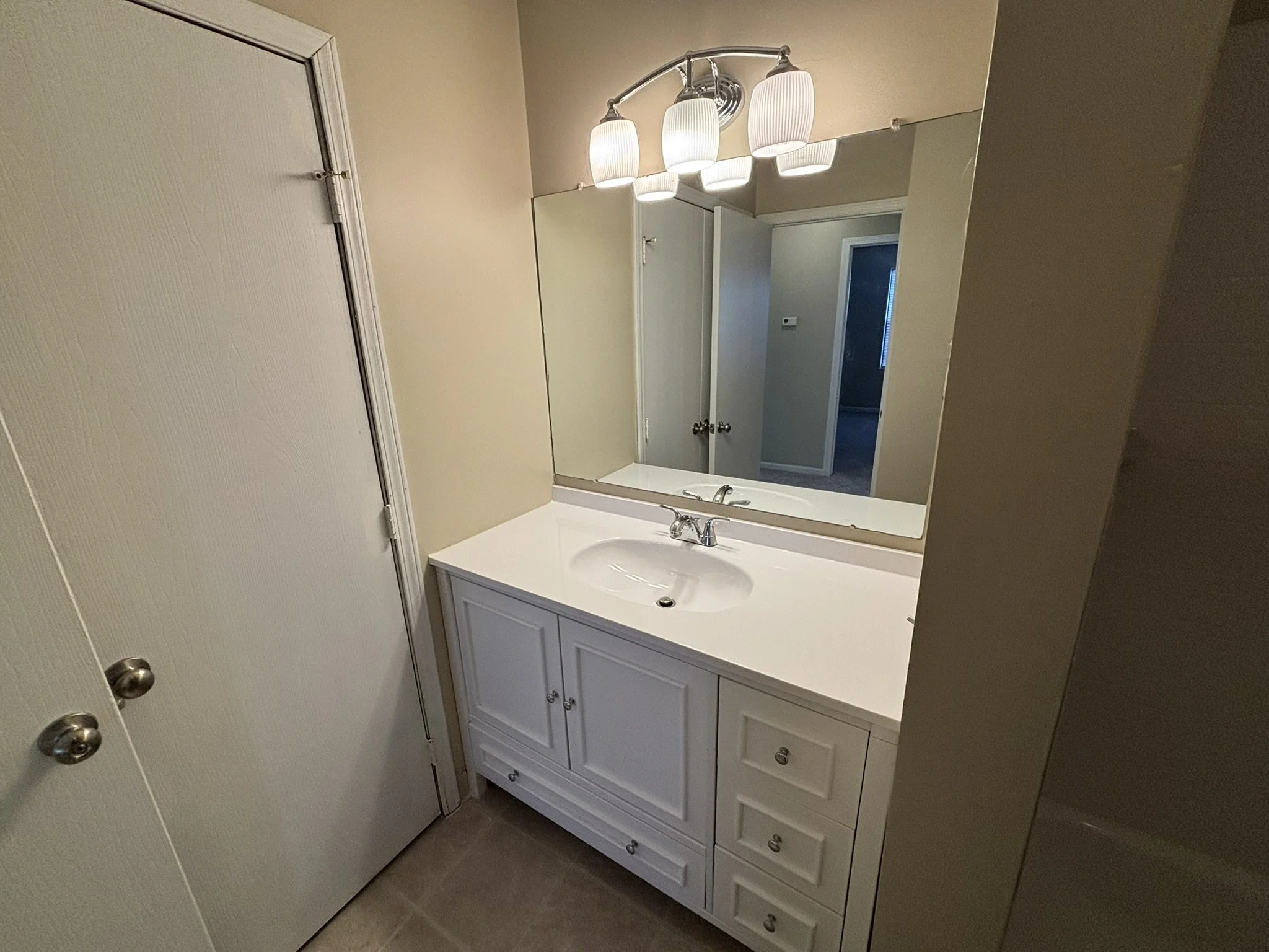Bathroom vanity with a white countertop, sink, and mirror, above a cabinet with drawers and doors, illuminated by a four-light ceiling fixture.