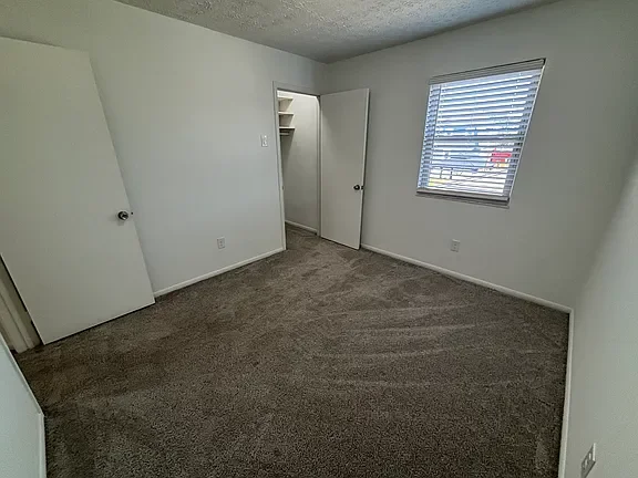 Empty bedroom with carpeted floor, white walls, a window with blinds, and a door leading to a closet.