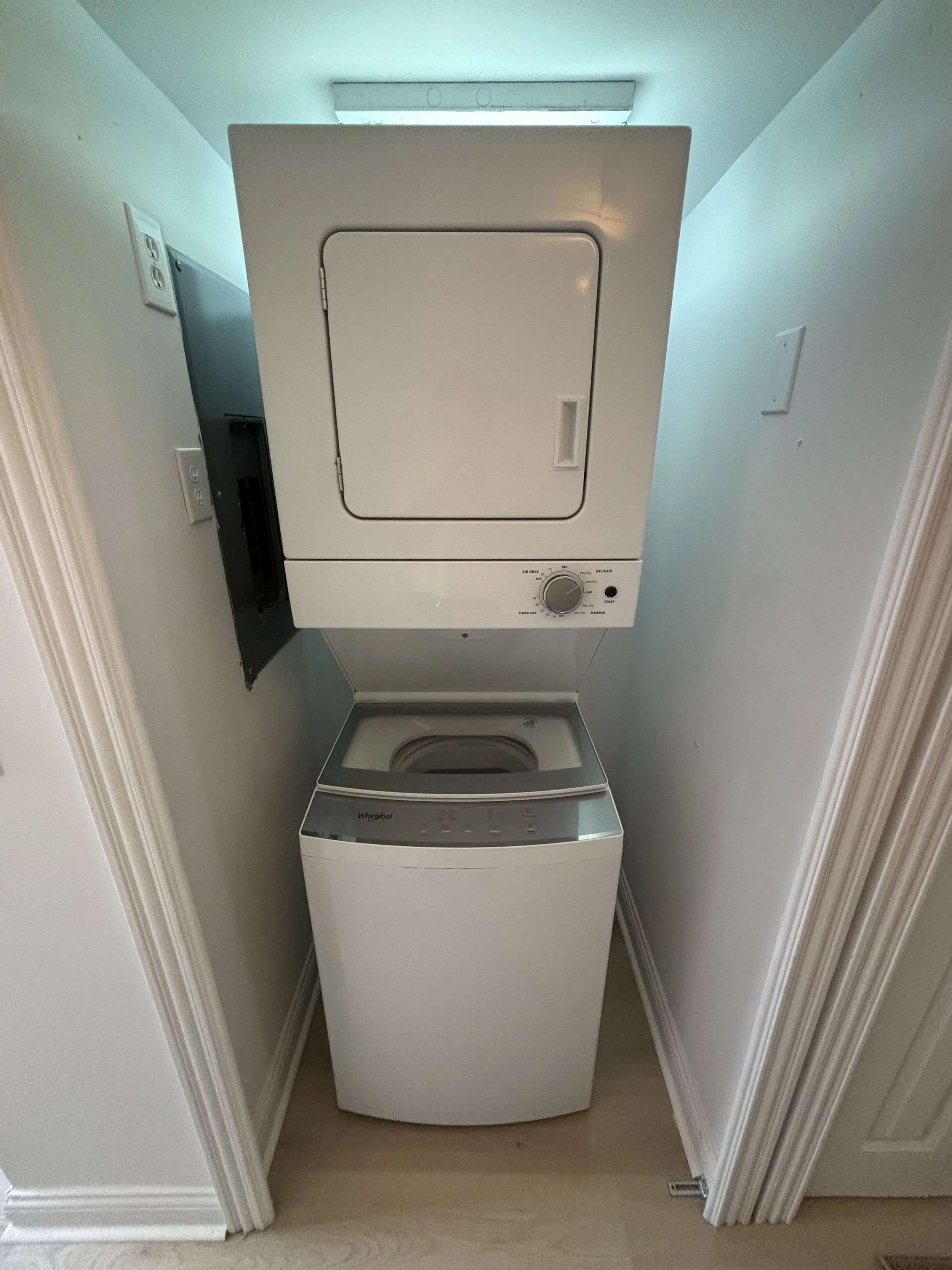 A stacked washer and dryer unit in a small laundry closet with white walls and a light-colored wood floor.