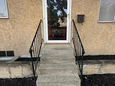 Concrete steps with black metal railings leading to a glass door in a beige stucco wall, with a window to the right.