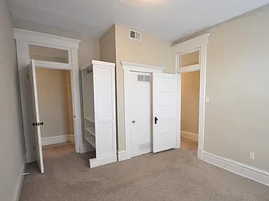 Empty room with beige walls, white trim, new trim work, and two open doors leading to other rooms.