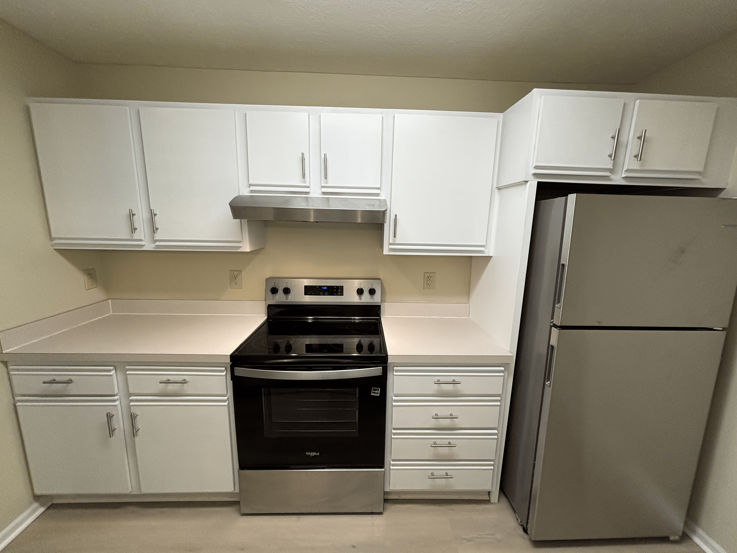 White kitchen cabinets, black oven, stainless steel range hood, stainless steel refrigerator.