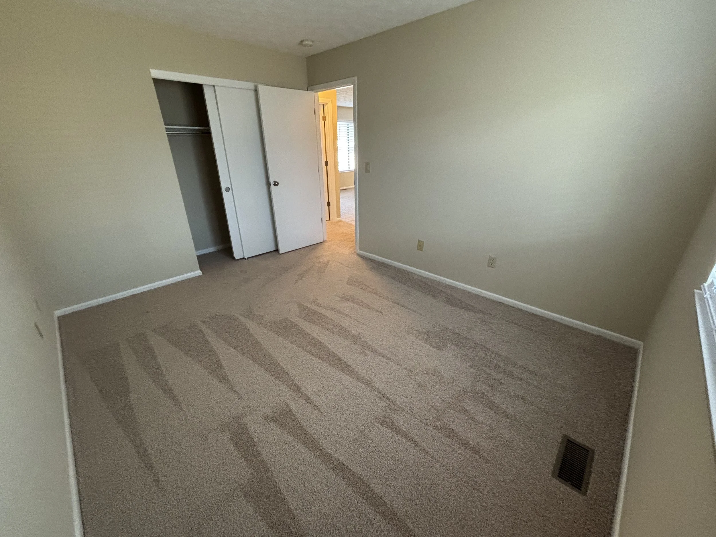 Empty bedroom with beige carpet, closet with sliding doors, and a window.