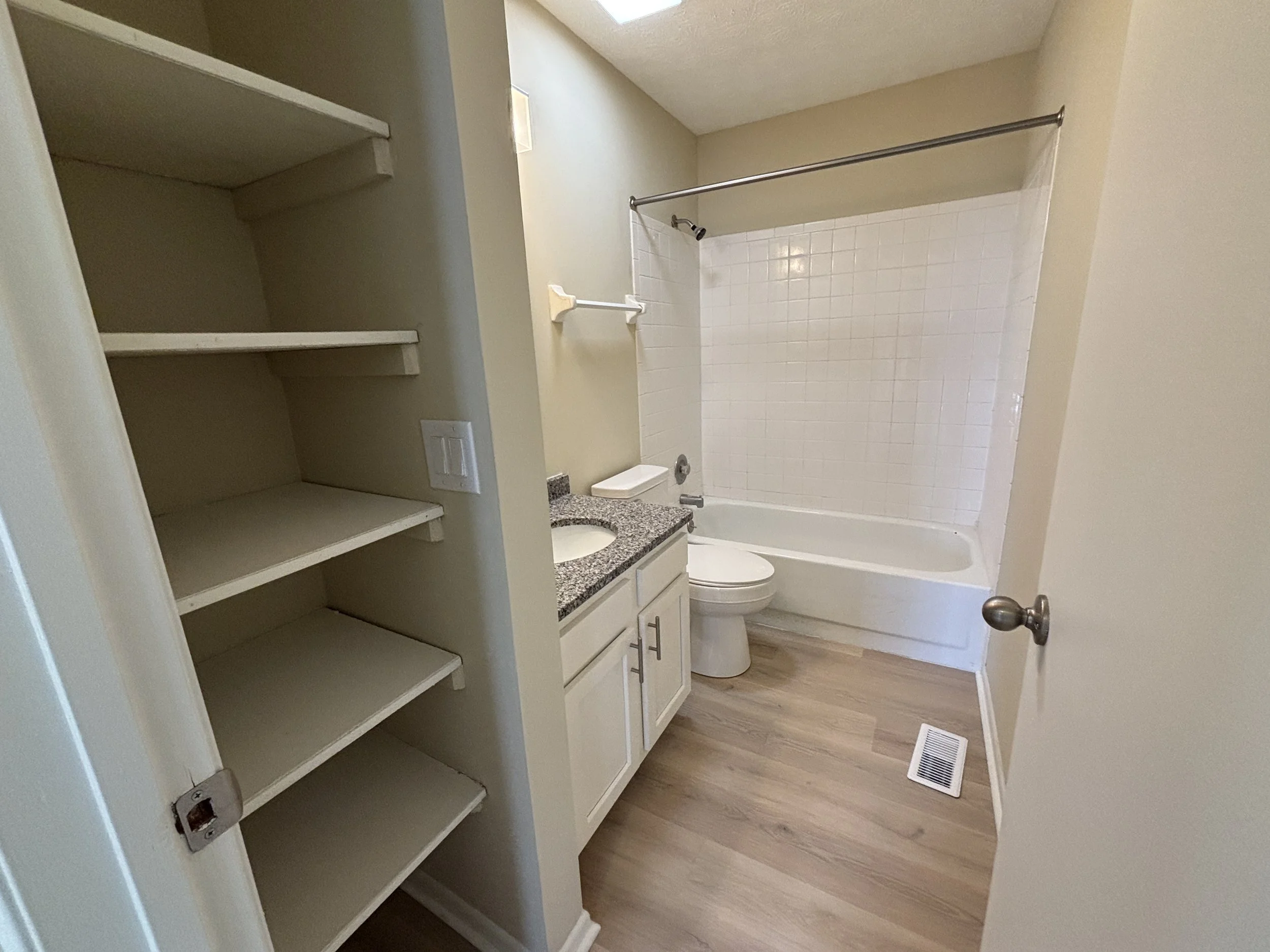 Bathroom with open shelving, granite countertop vanity, toilet, bathtub with shower curtain, and wood-style flooring.