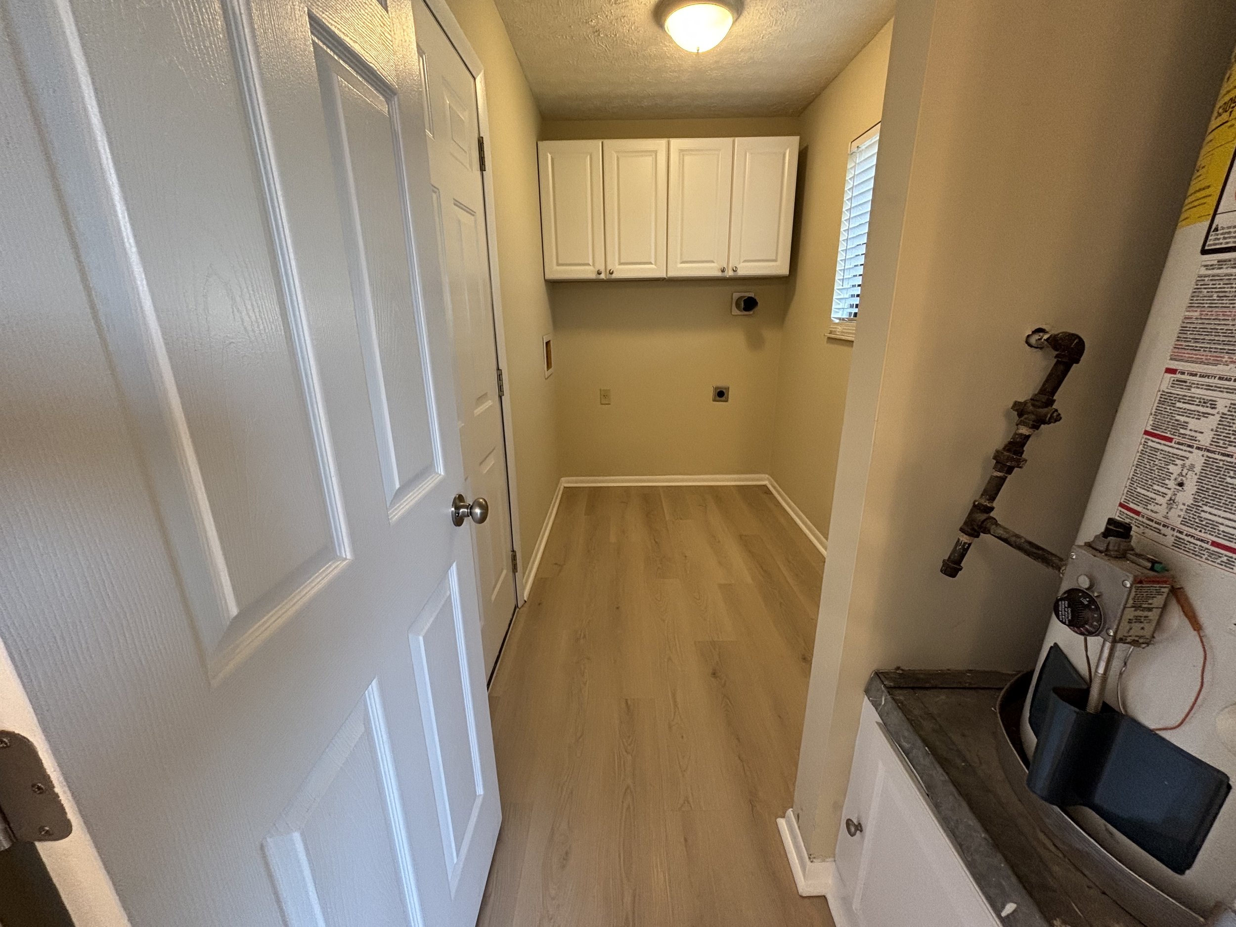 Empty laundry room with white cabinets, wooden floor, and a water heater on the right side.