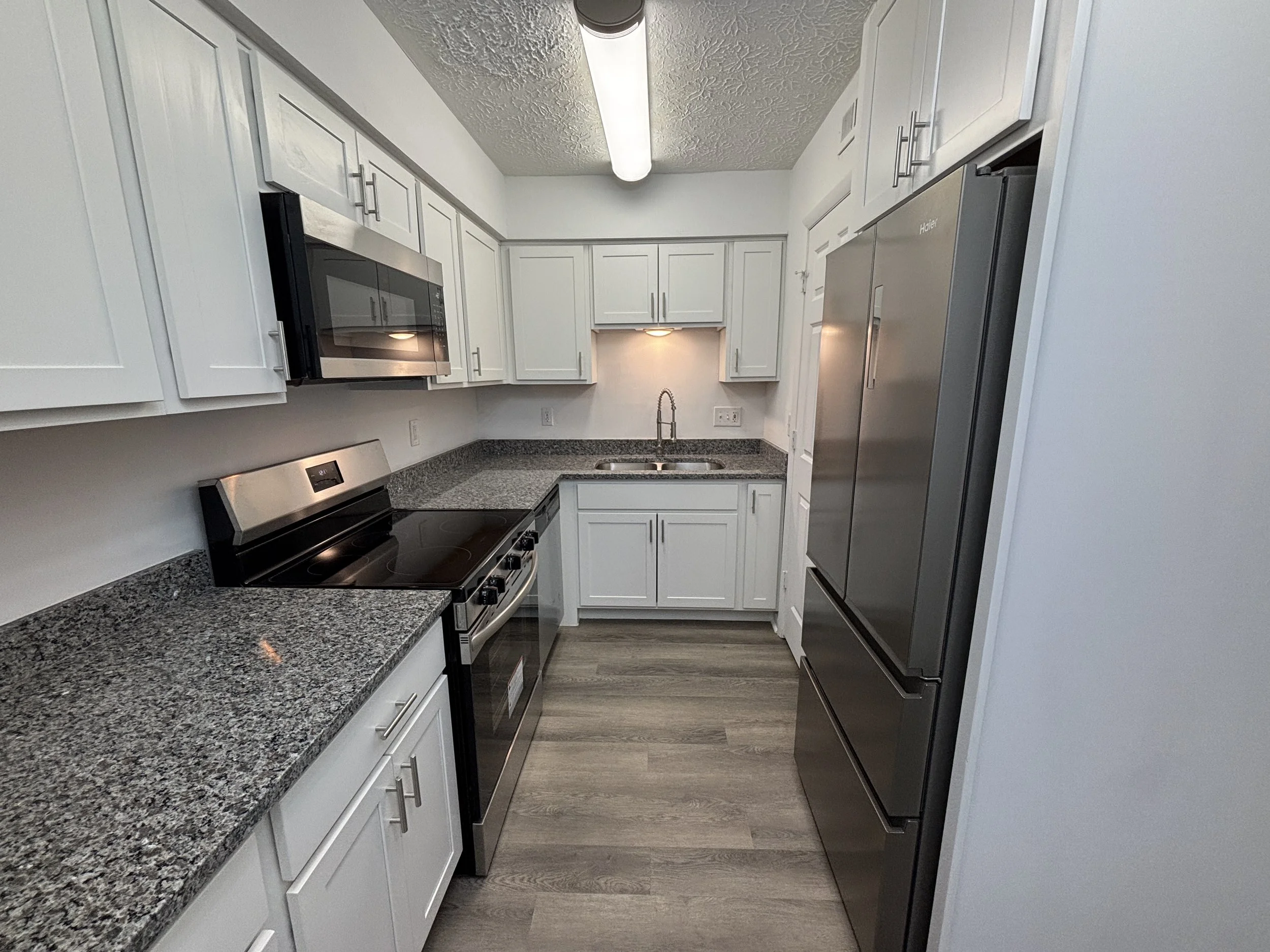 Kitchen with white cabinets, granite countertops, stainless steel appliances, and laminate wood flooring.