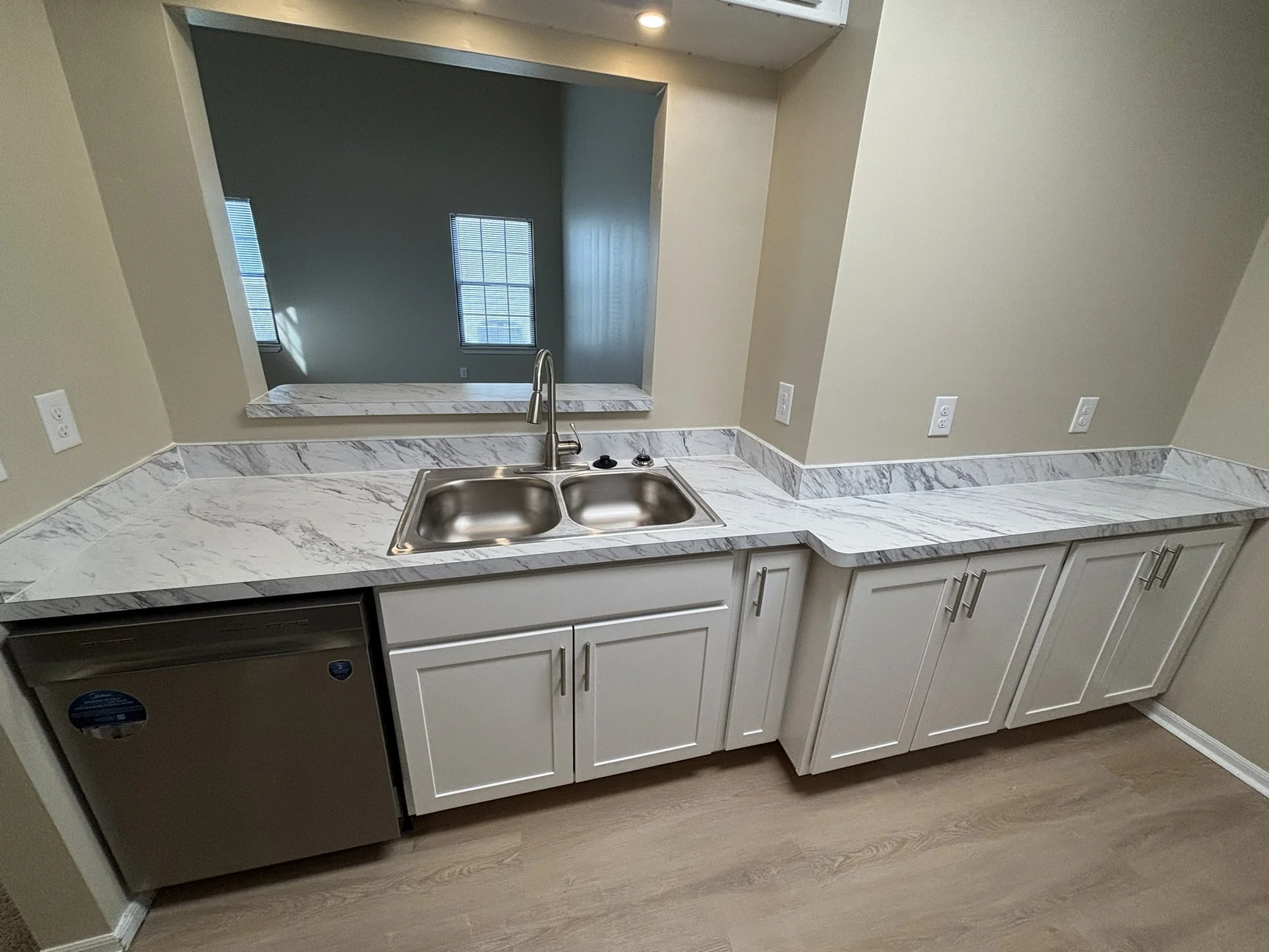 Kitchen counter with white marble surface, stainless steel sink, and white cabinetry, with a pass-through window to an adjacent room.
