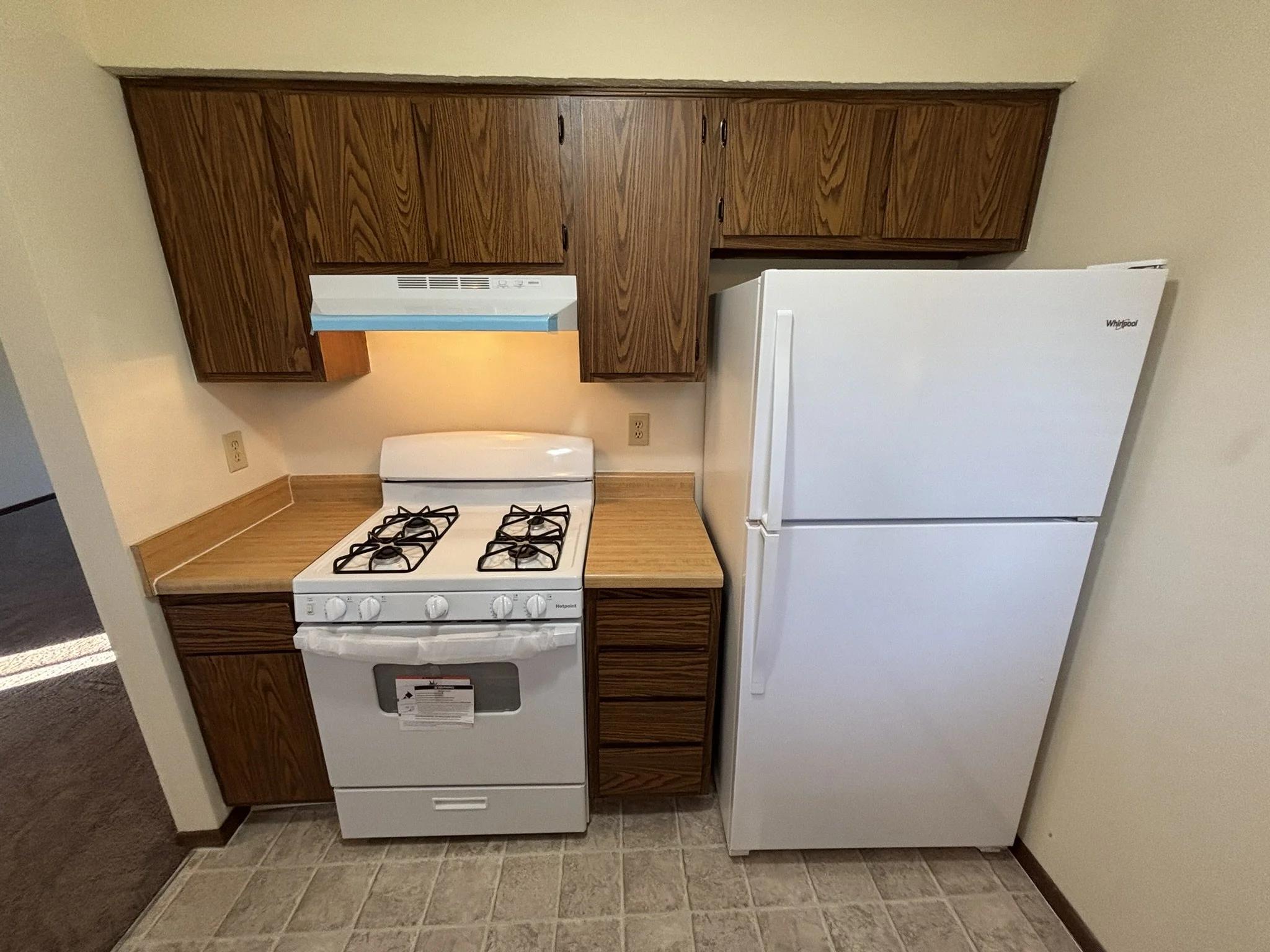Kitchen with wooden cabinets, a white gas stove, and a white refrigerator on a beige tiled floor.