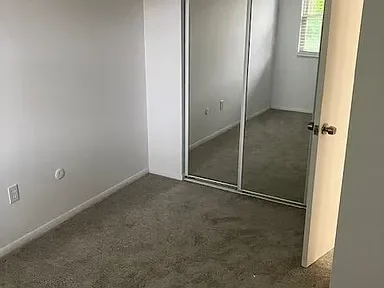 Empty bedroom with carpeted floor, mirrored closet doors, and a window