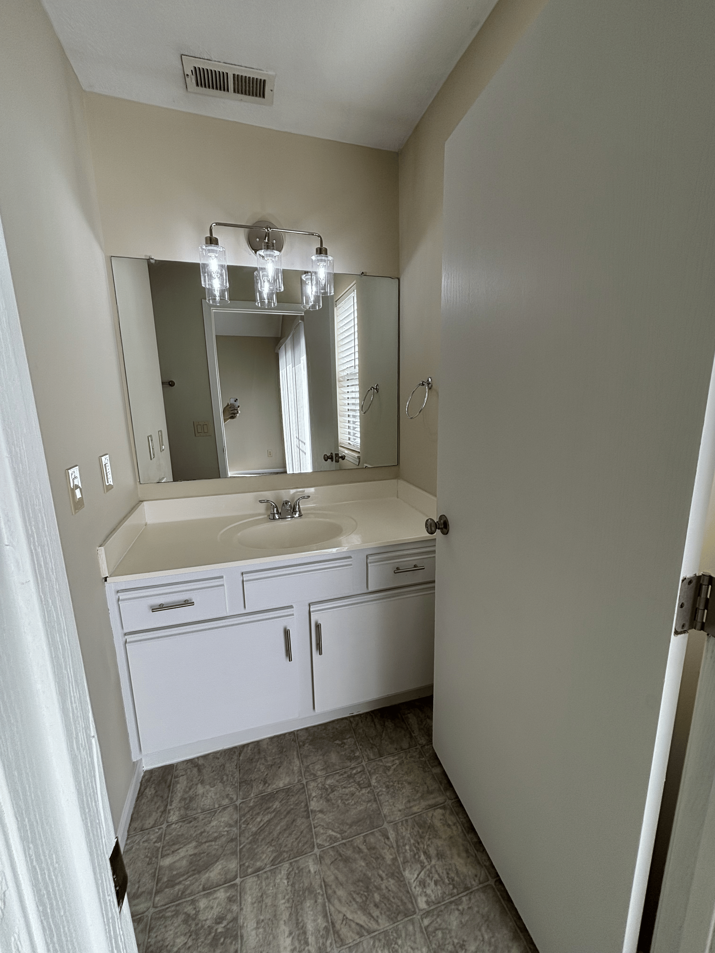Bathroom with a white vanity, mirror, wall-mounted lights, and beige walls.