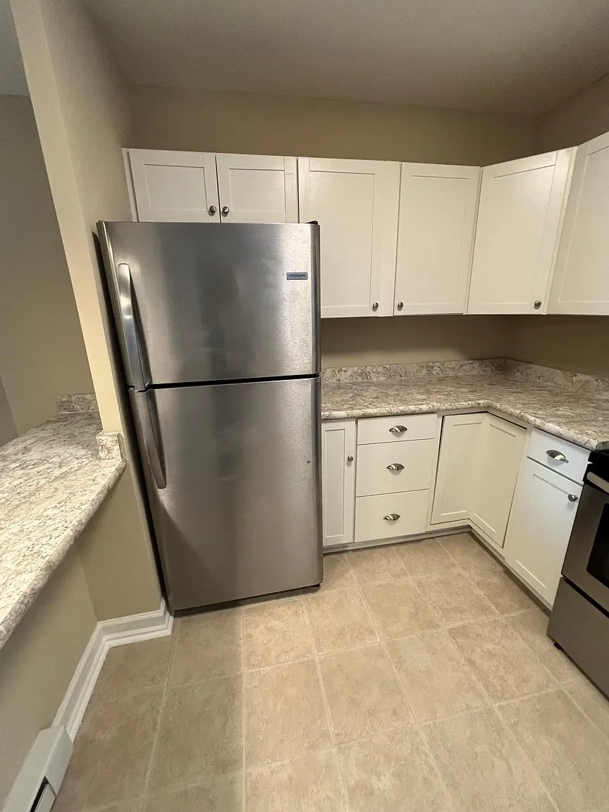 Kitchen with white cabinets, granite countertops, beige tile floor, stainless steel refrigerator, and a stove.