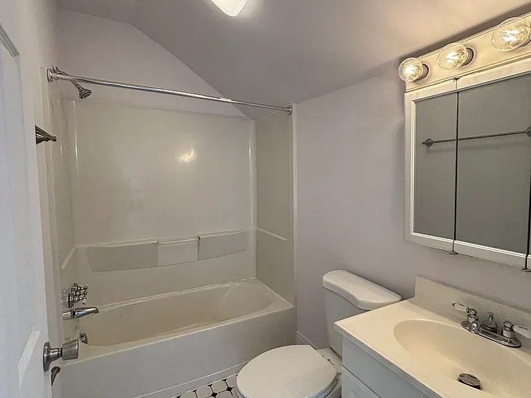 Bathroom with bathtub, shower curtain rod, toilet, sink, and mirror with light bulbs.
