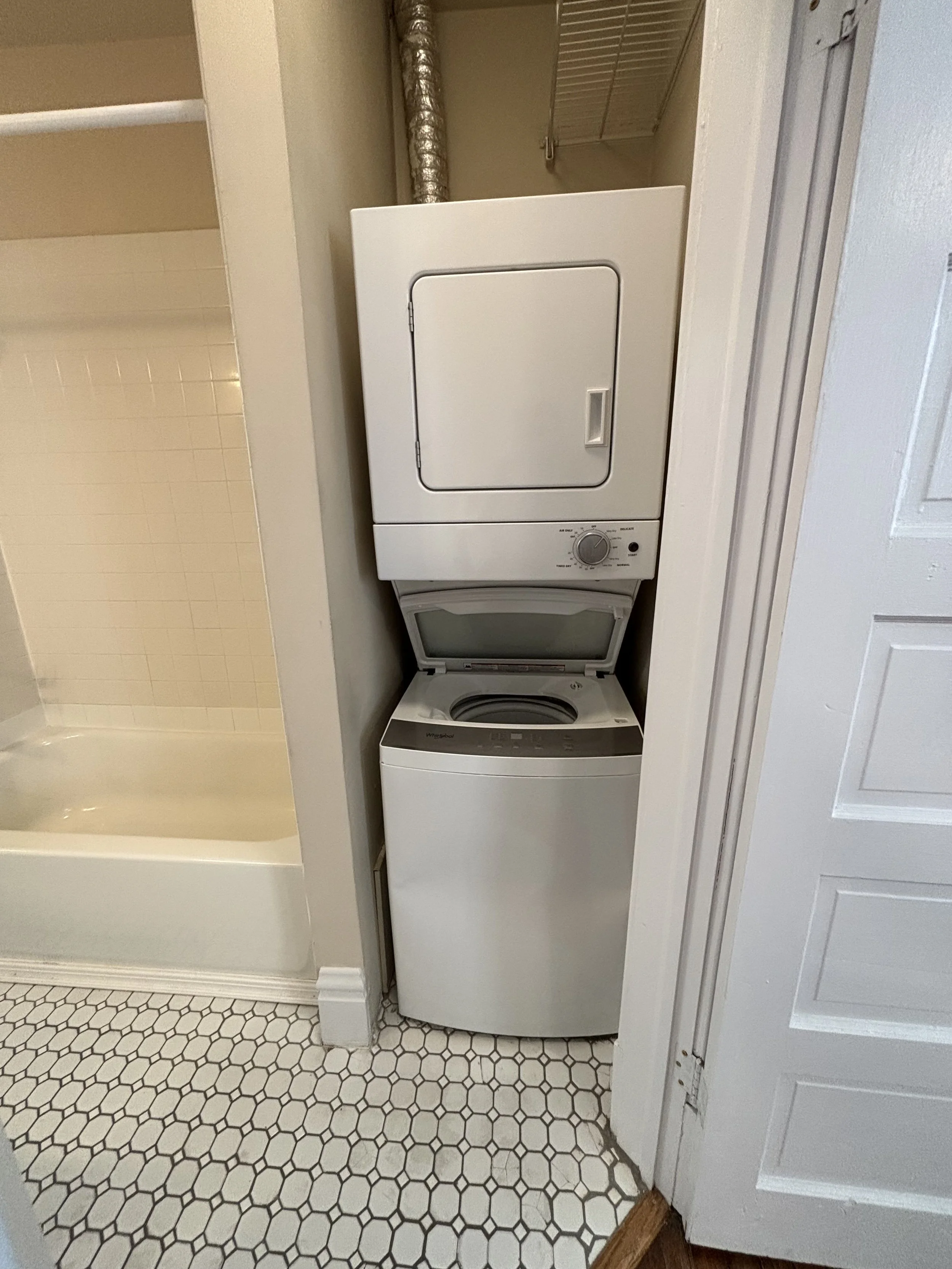 A stacked white washer and dryer unit in a small laundry area with hexagon-shaped floor tiles.