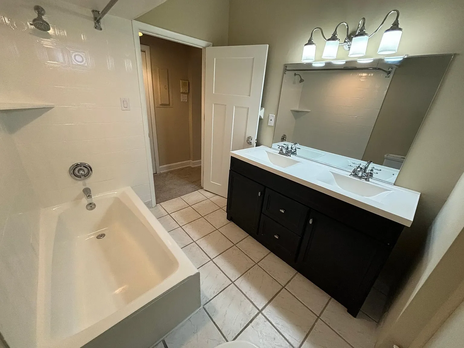 Bathroom with a bathtub, double sink vanity with mirror, and a wall-mounted light fixture.