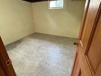 Empty room with beige walls, tiled floor, a small window, and a partially open wooden door.