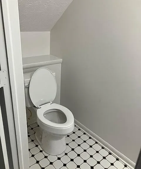 Toilet in a small bathroom with gray walls and a black and white hexagon tile floor.