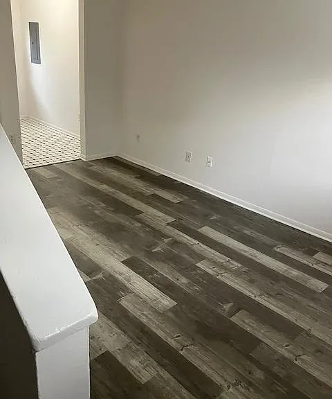 Empty room with dark wood floor and white walls, open doorway to a small entryway with a patterned tile floor.