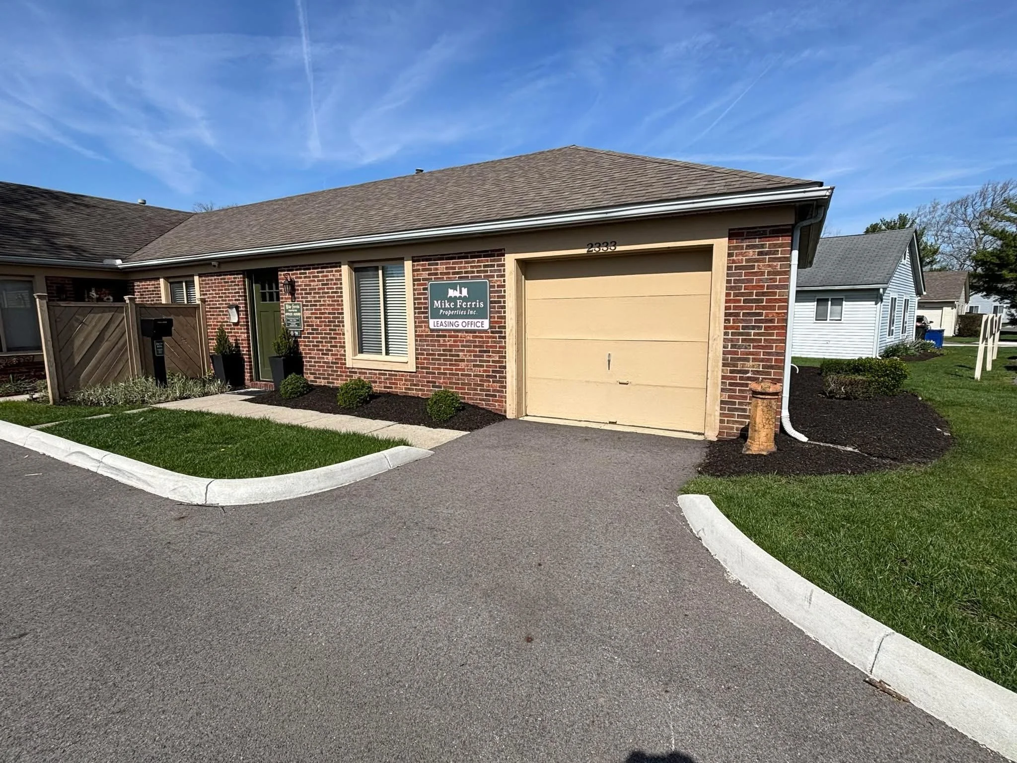 A brick residential building with a beige garage door and a sign for Mike Ferris Properties Inc. Leasing Office.