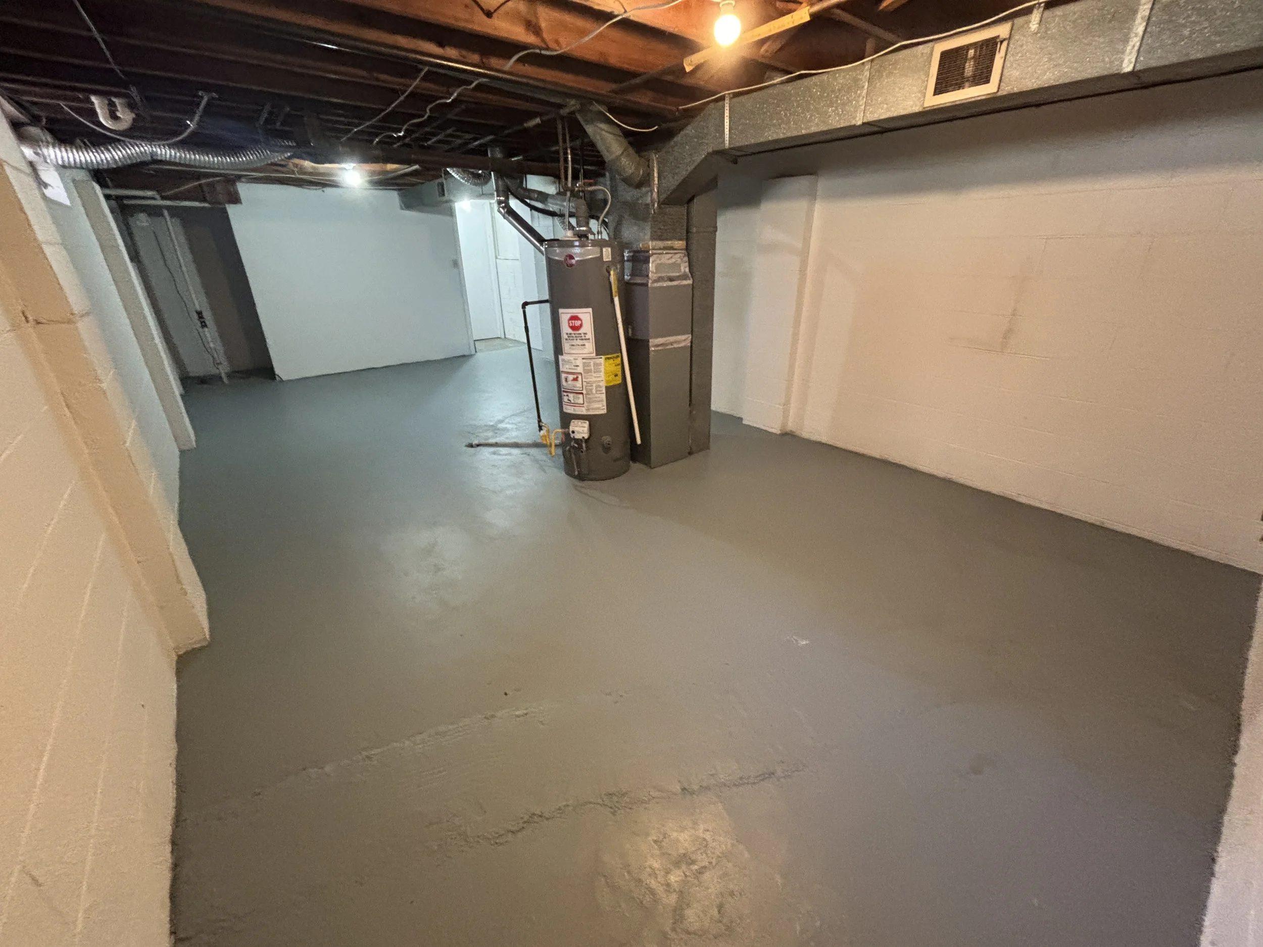 View of an unfinished basement with concrete floor, utility area, water heater, pipes, and staircase leading up.