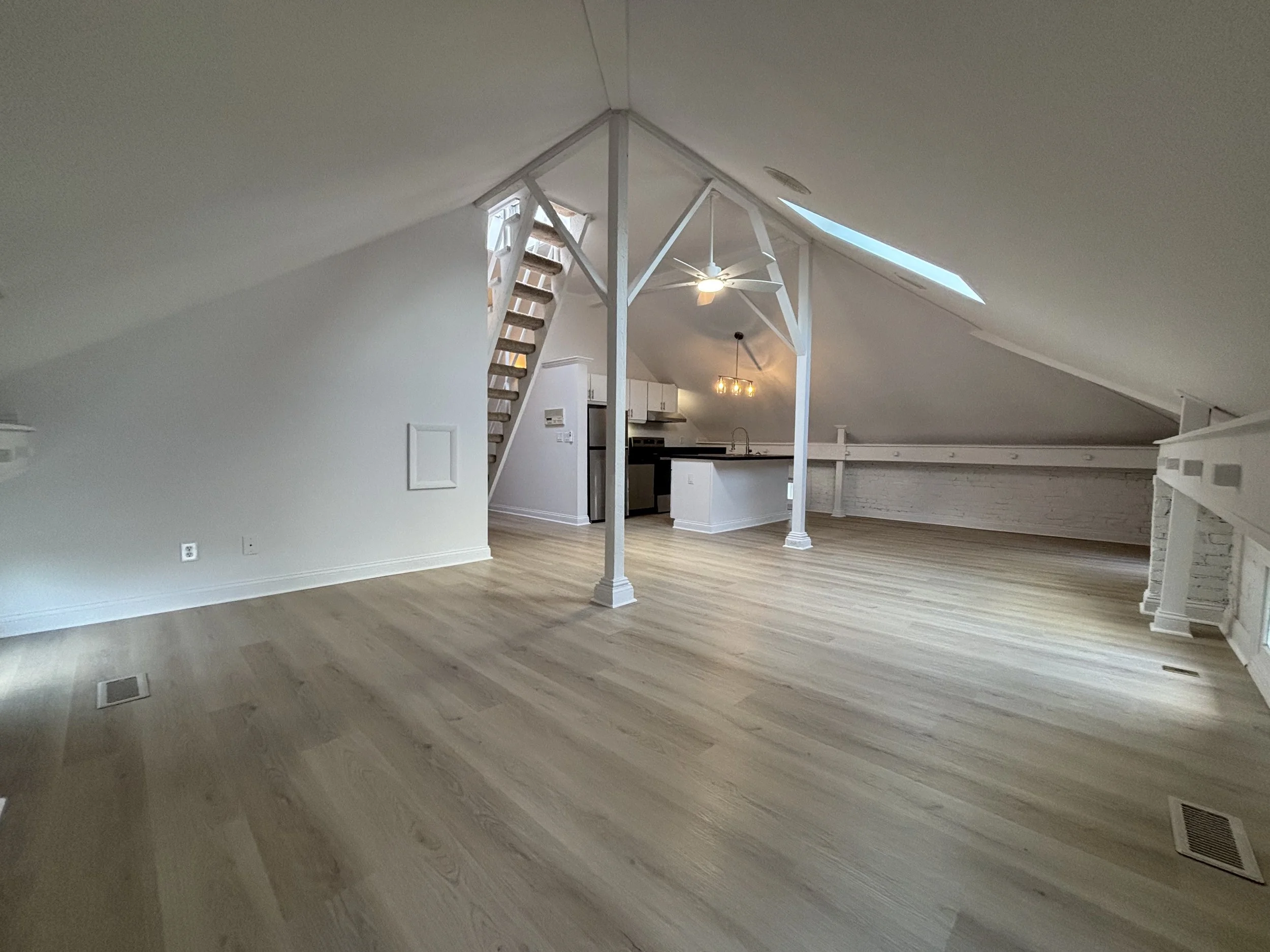 Spacious attic apartment with sloped ceilings, wooden flooring, skylights, staircase, and open kitchen area.