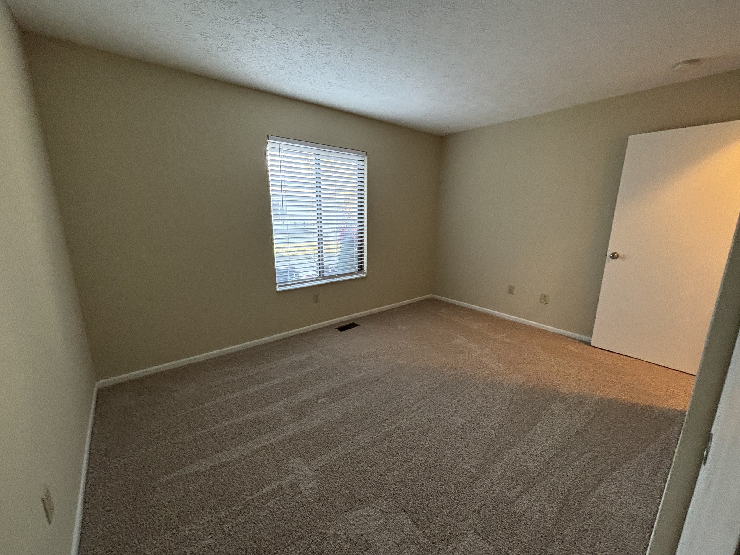 Empty room with beige walls, a window with blinds, and carpeted floor.