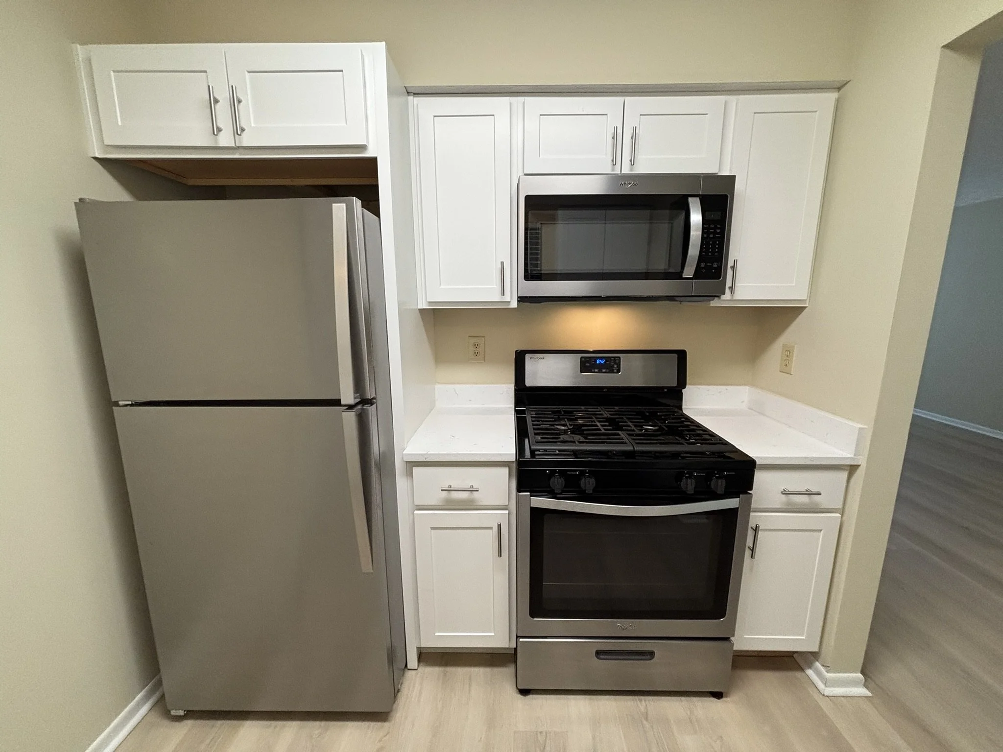 Kitchen with stainless steel refrigerator, white cabinets, black gas stove, and microwave above stove.